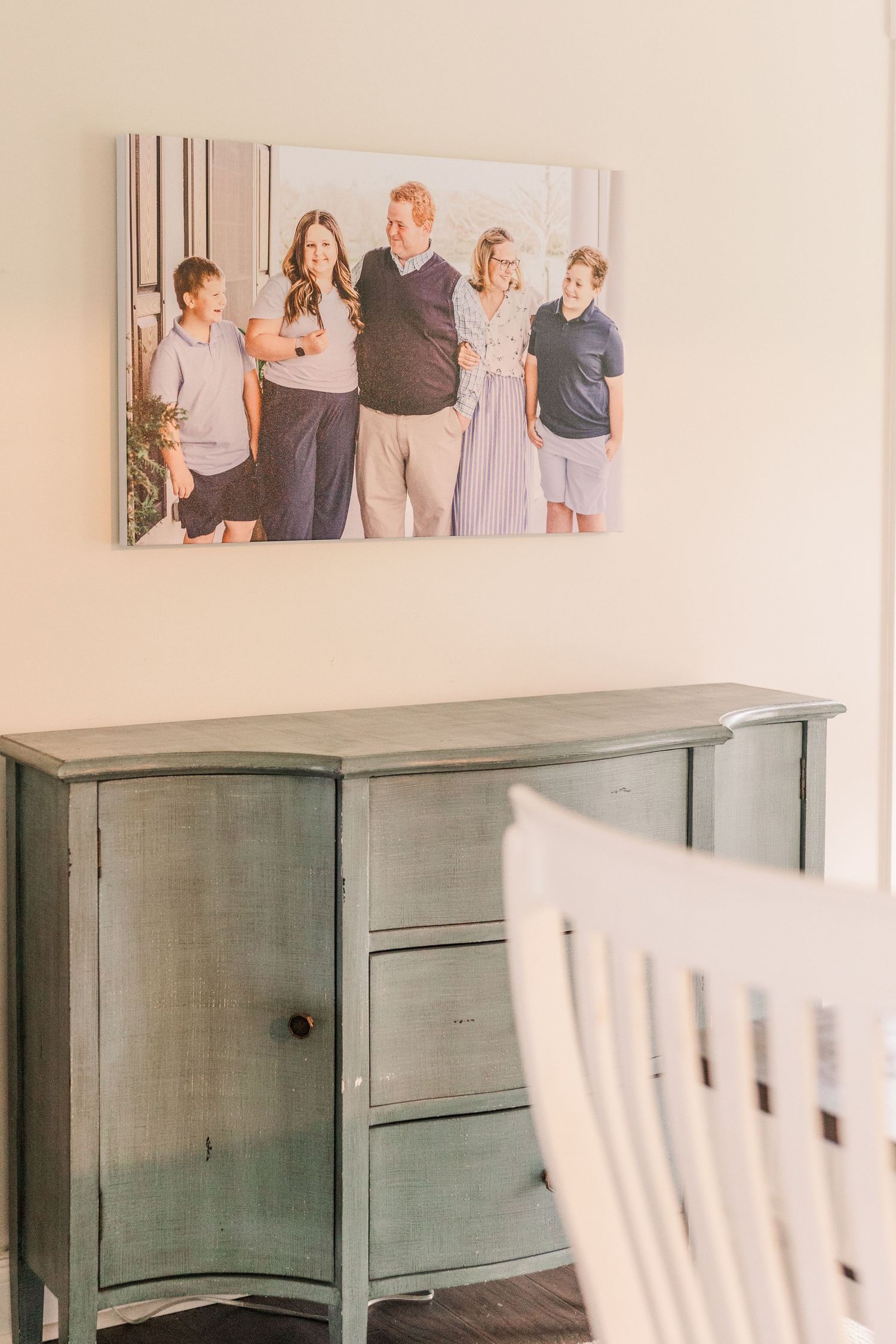 A gray painted dresser sits beneath a family photograph on a beige wall in a home interior.