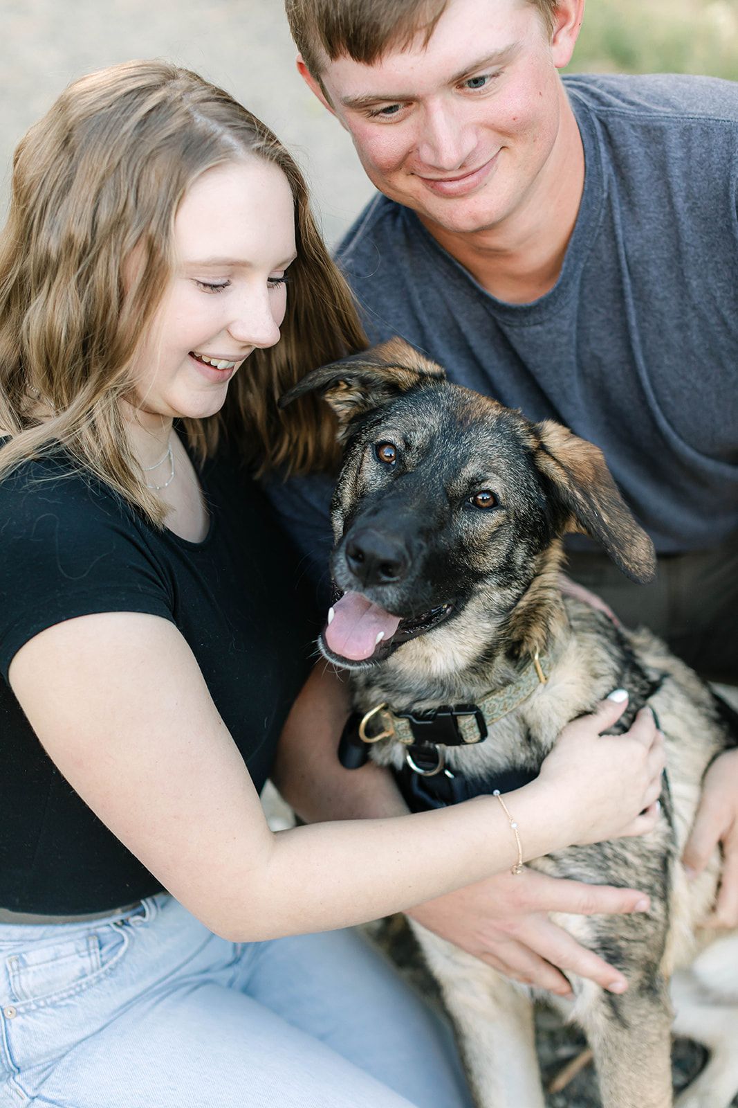 Happy couple cuddling with their German Shepherd dog outdoors.