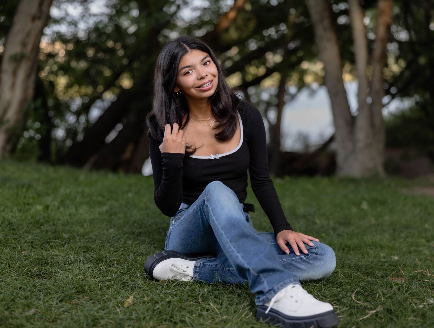 Casual lifestyle portrait of person sitting on grass wearing jeans and white sneakers.
