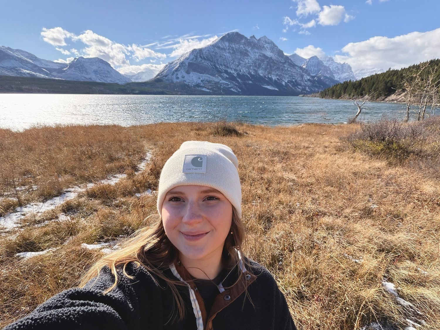 A stunning mountain lake landscape with snowy peaks and brown winter grass in the foreground.
