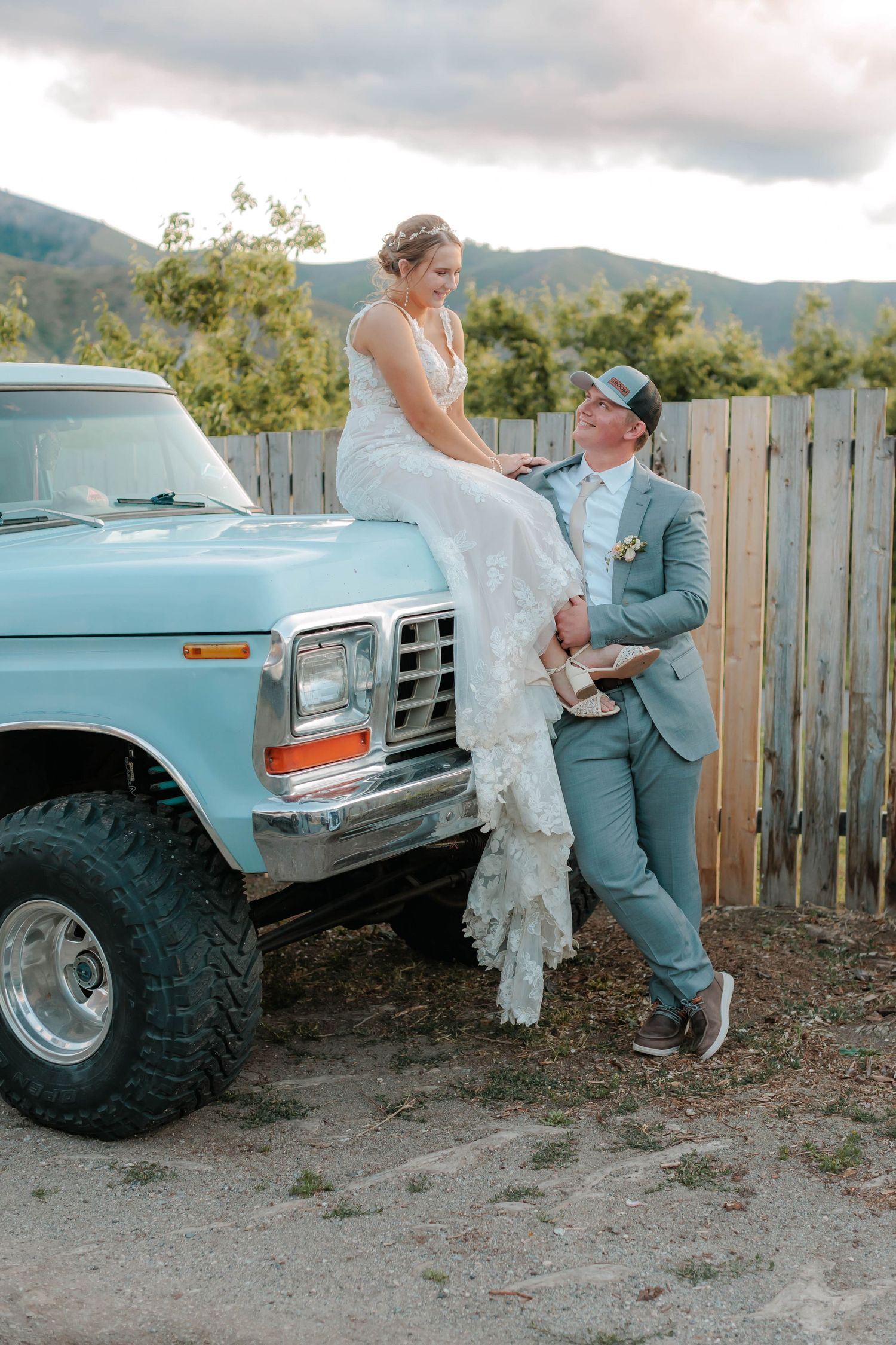 Wedding couple poses with vintage blue pickup truck against mountain backdrop.