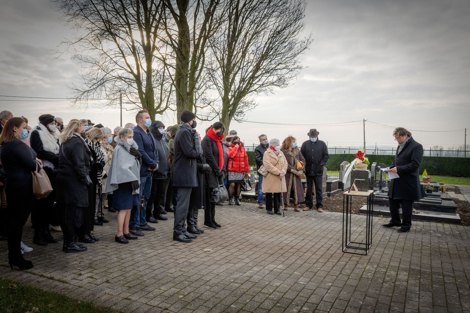 Group of people gathered outdoors at a memorial ceremony near a podium on a cloudy day.