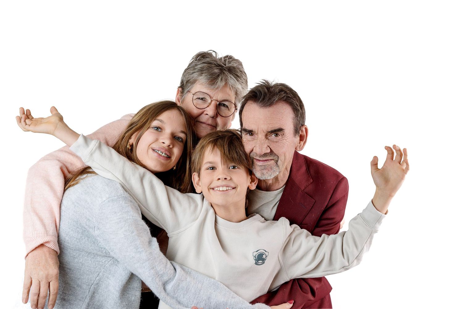 A family of four poses together in casual clothing against a white background while making silly expressions.
