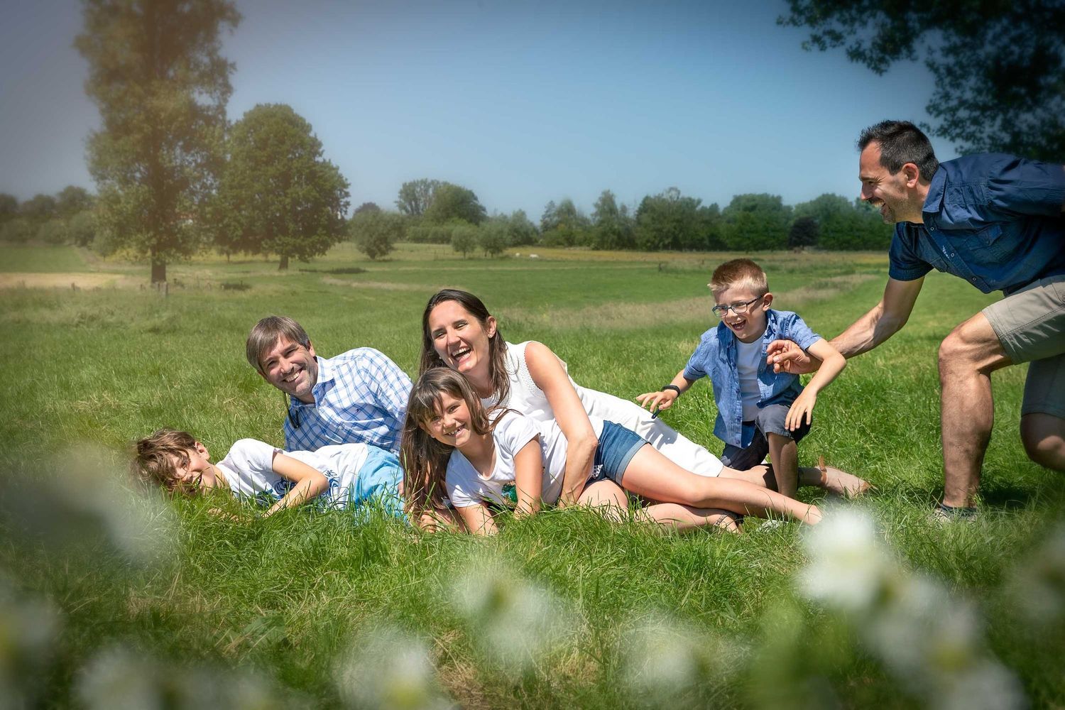 Group enjoying a playful moment while lying in a sunny meadow with wildflowers and trees in the background.