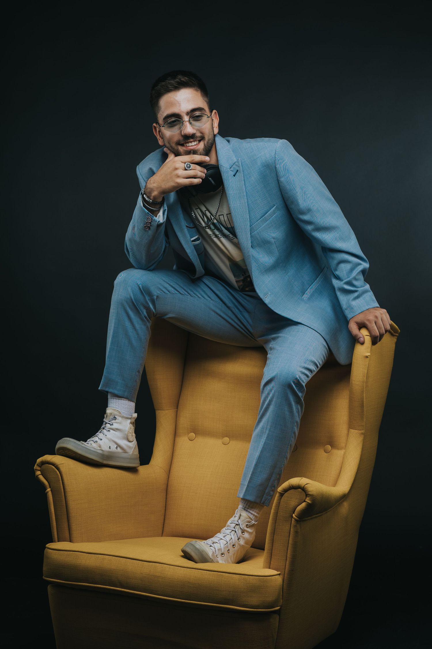 Stylish portrait of person in light blue suit posing on yellow armchair.