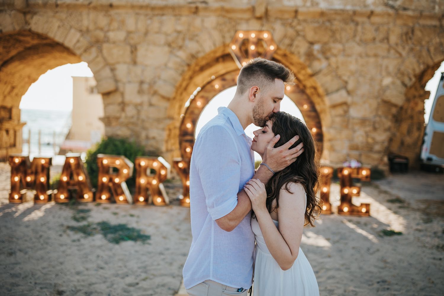 A romantic moment between a couple in a rustic courtyard with illuminated letters.