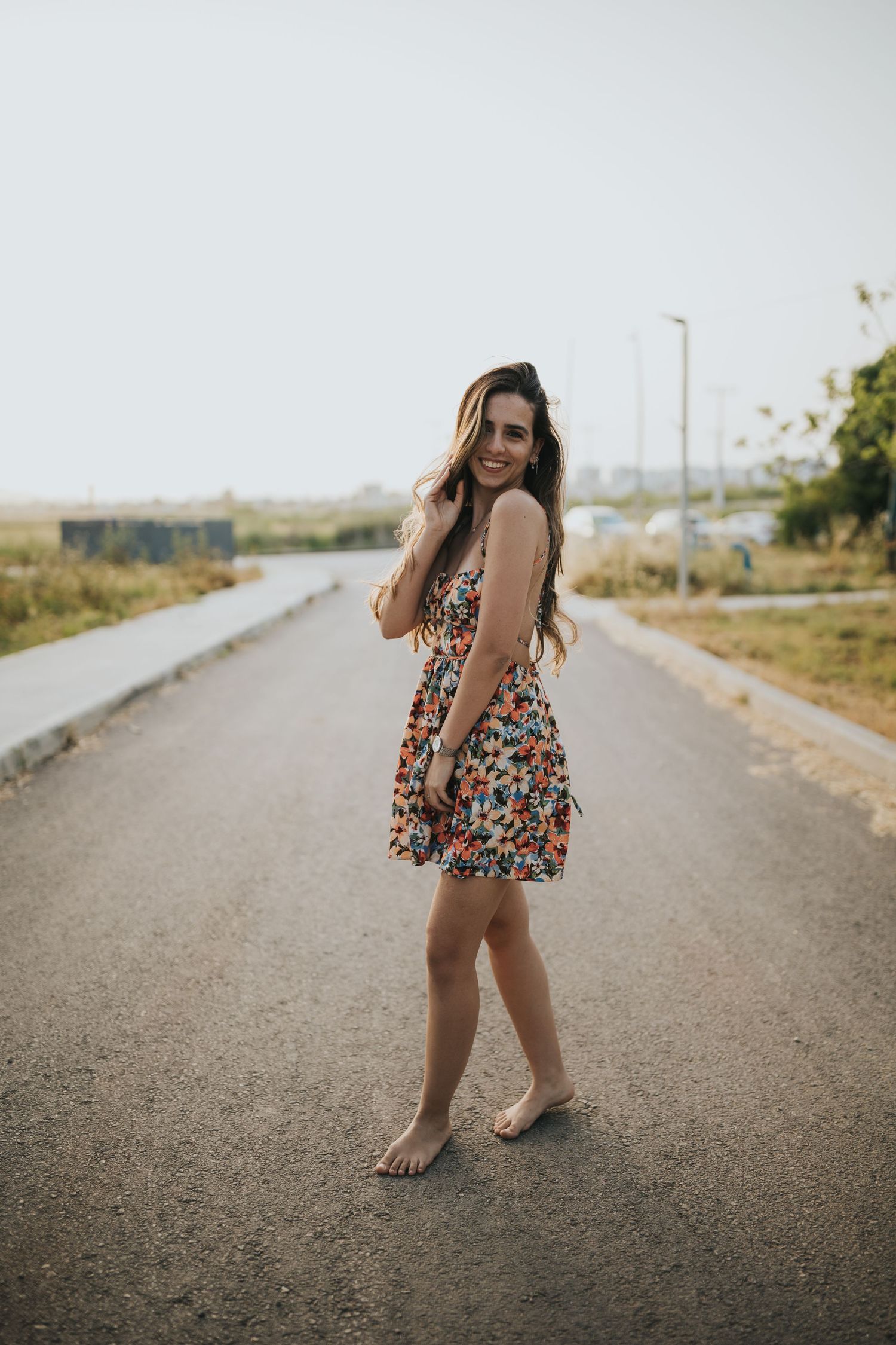 Carefree pose in floral summer dress on empty rural road.