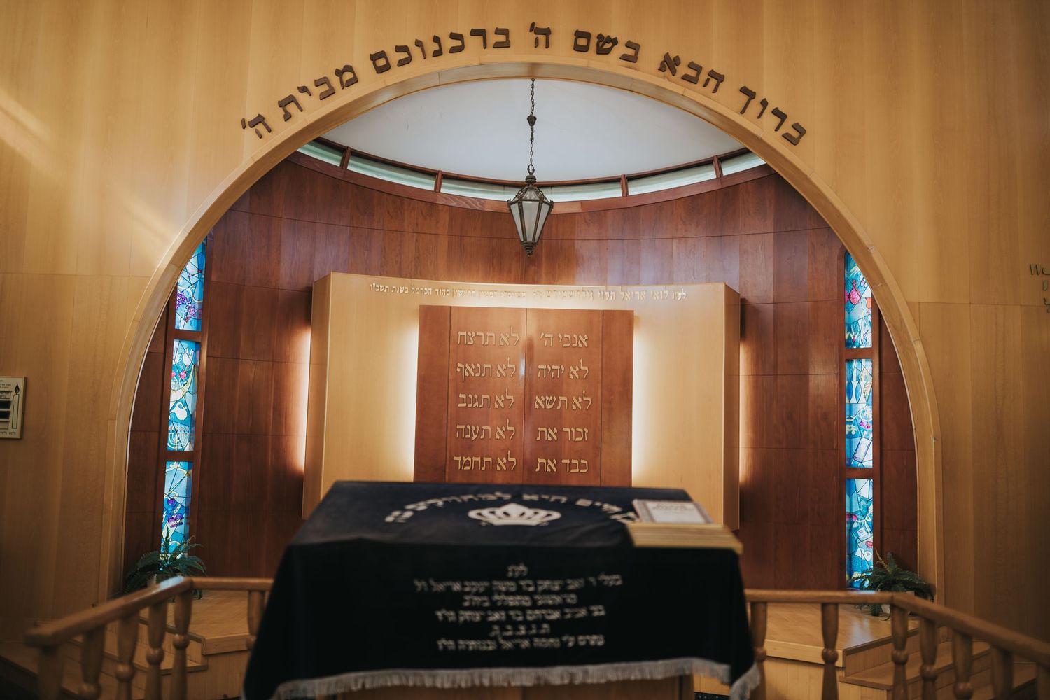 Interior view of a synagogue showing an ornate archway with Hebrew text and altar.
