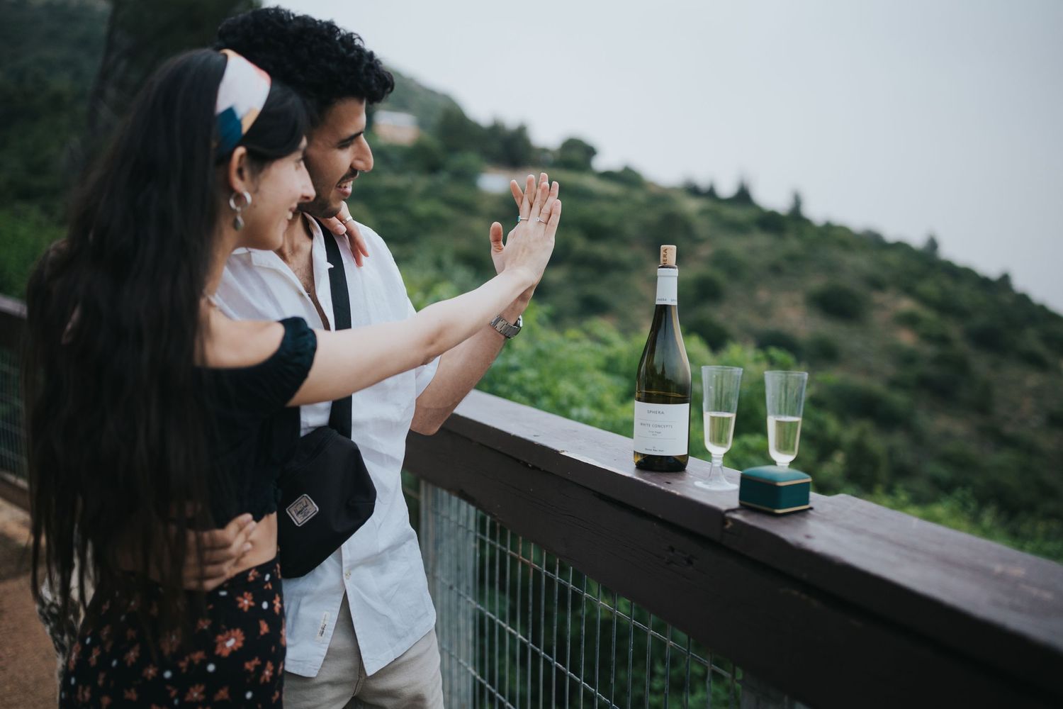 Couple celebrating with champagne on outdoor terrace overlooking scenic hills.