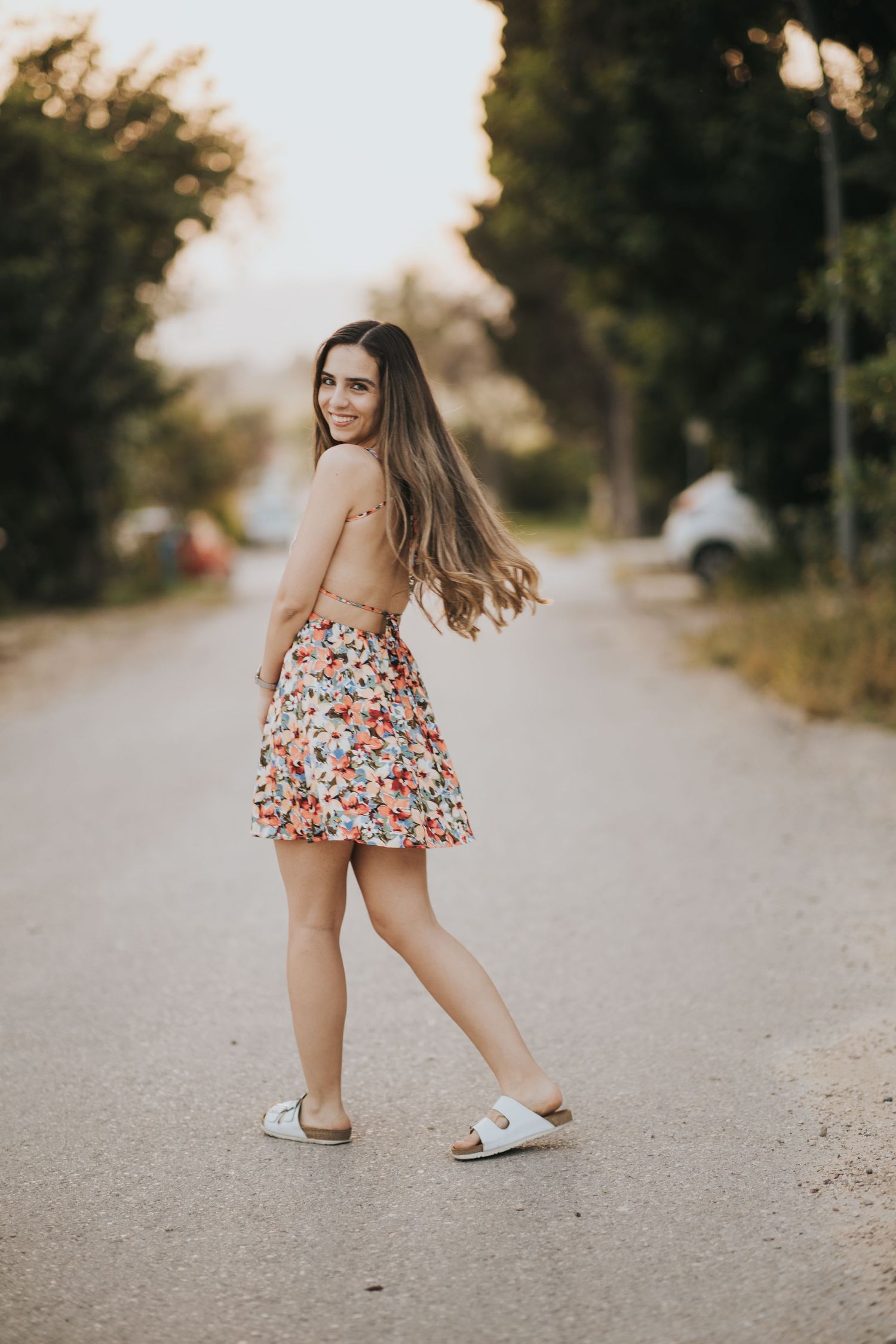 Playful twirl in floral sundress on sunset-lit country road.