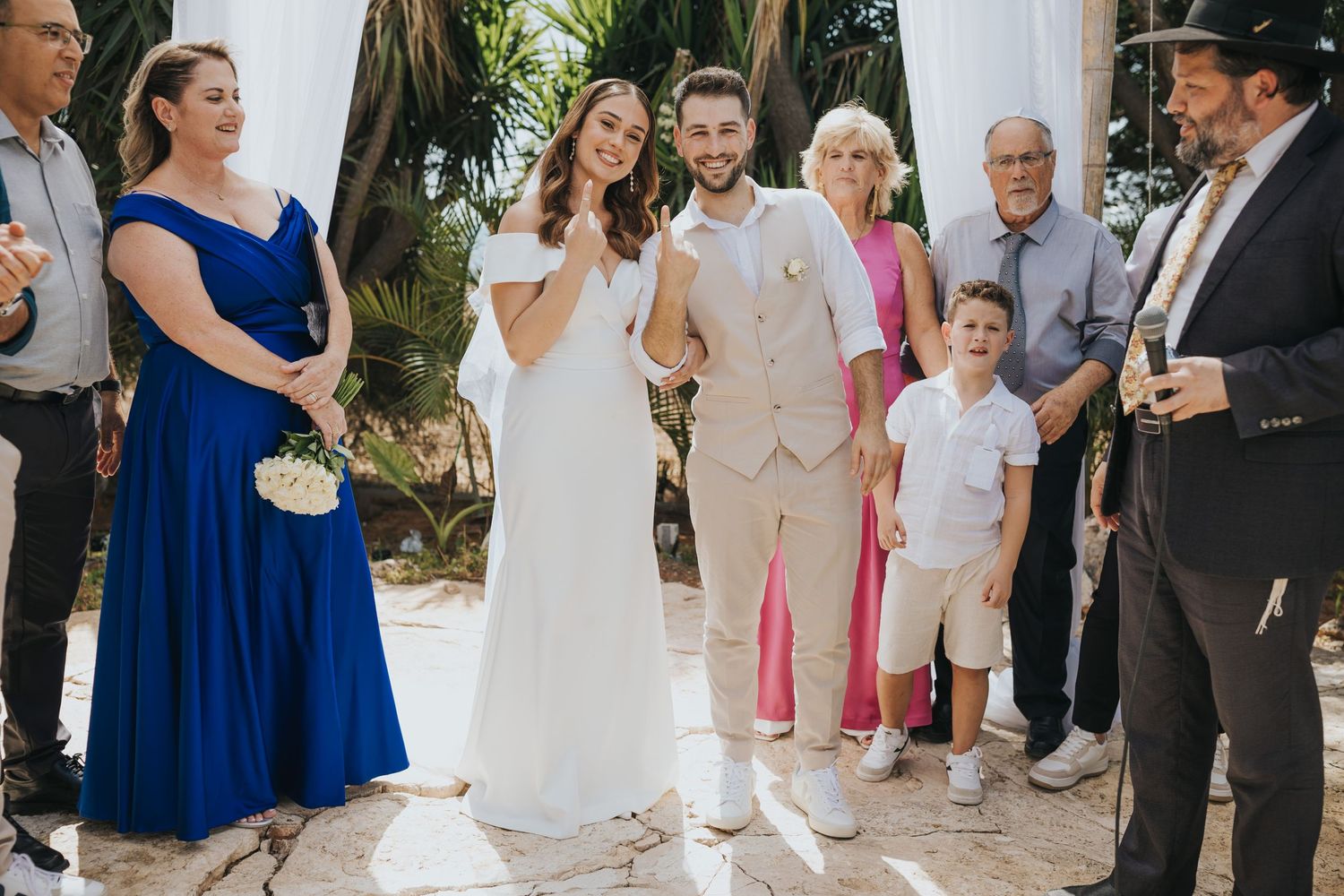 Outdoor wedding ceremony with guests gathered around couple in white and blue attire.