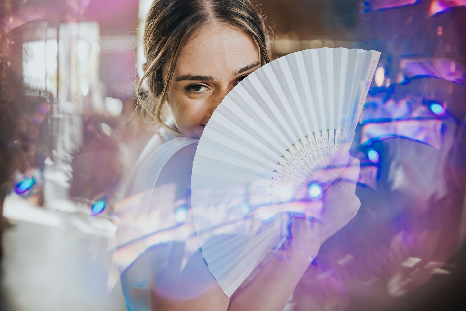 A white paper fan held up against purple party lighting creates an artistic effect.