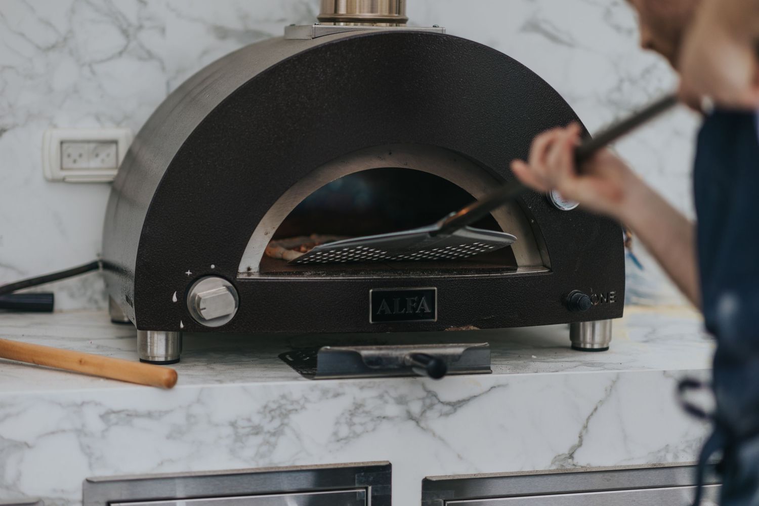 Black pizza oven with marble countertop being prepared for cooking.