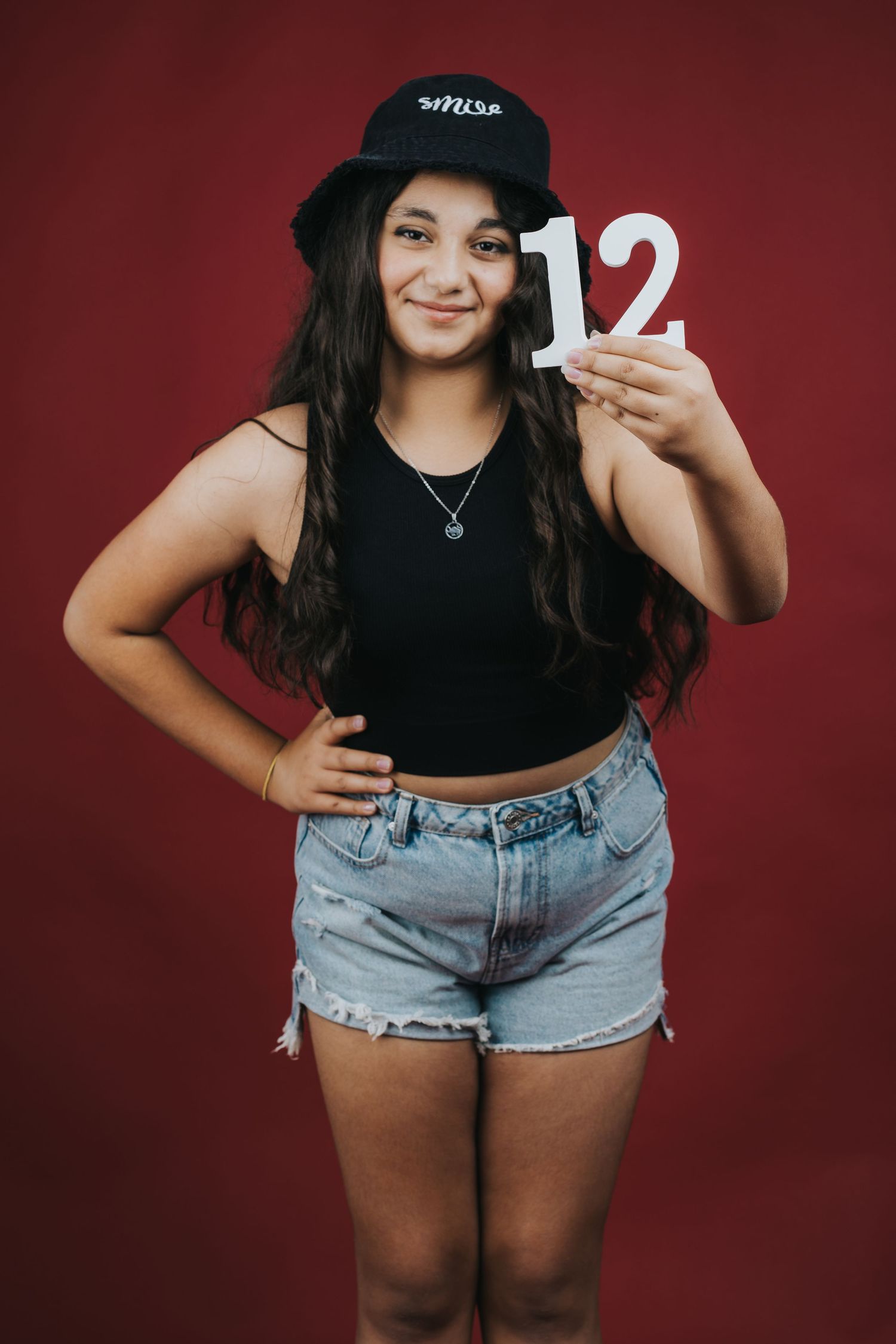 Casual fashion portrait with number 12 prop against burgundy background.