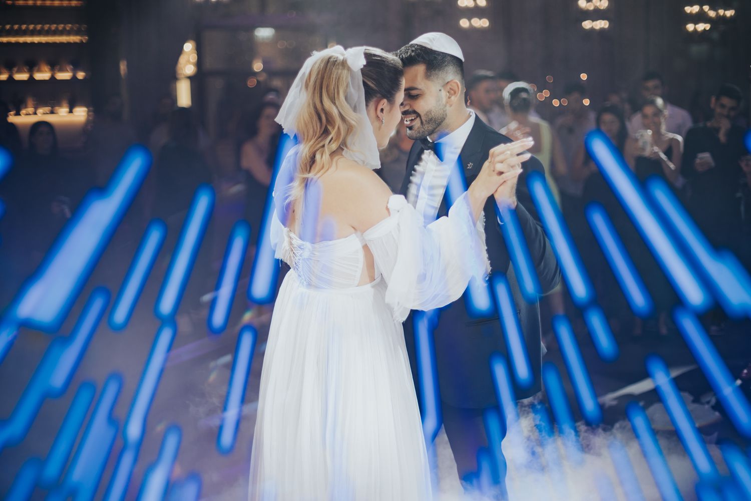 Couple shares their first dance surrounded by dramatic blue lighting effects on wedding dance floor.