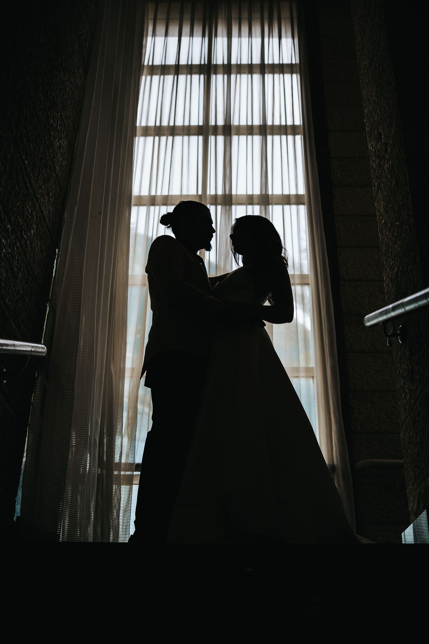 Silhouette of a couple against a tall window in a romantic pose.