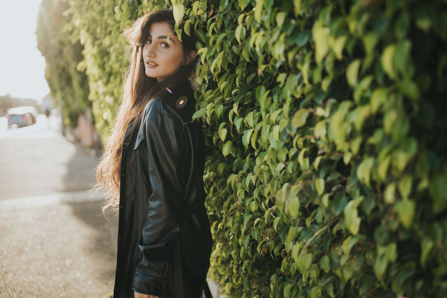Portrait against ivy wall wearing black leather jacket in natural lighting.