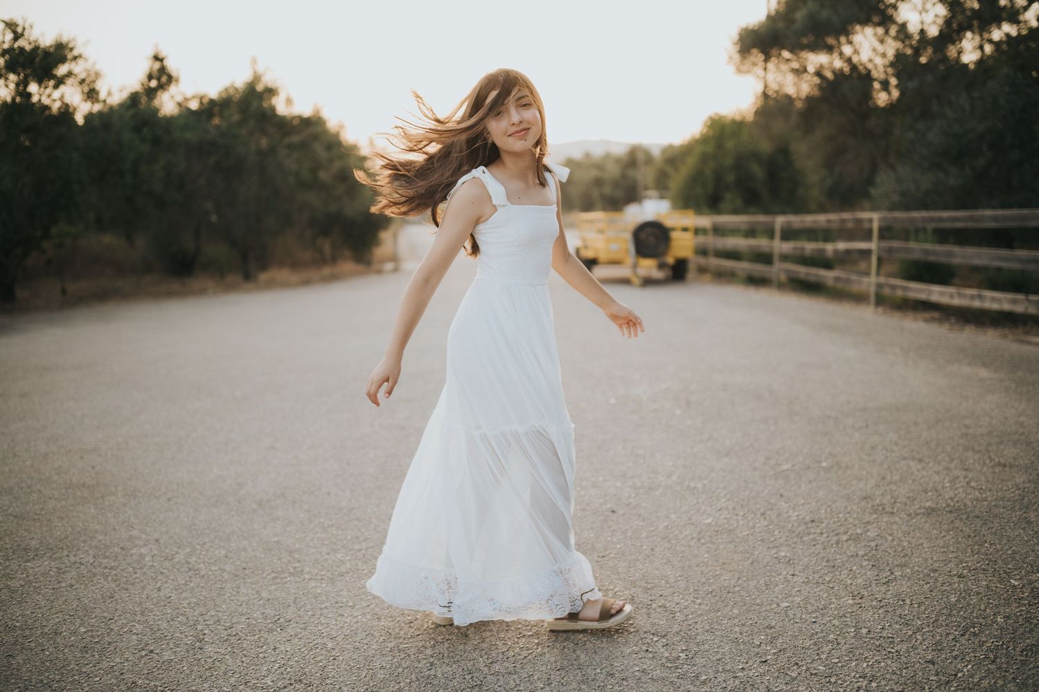 Woman in white dress twirling on rural road at sunset.