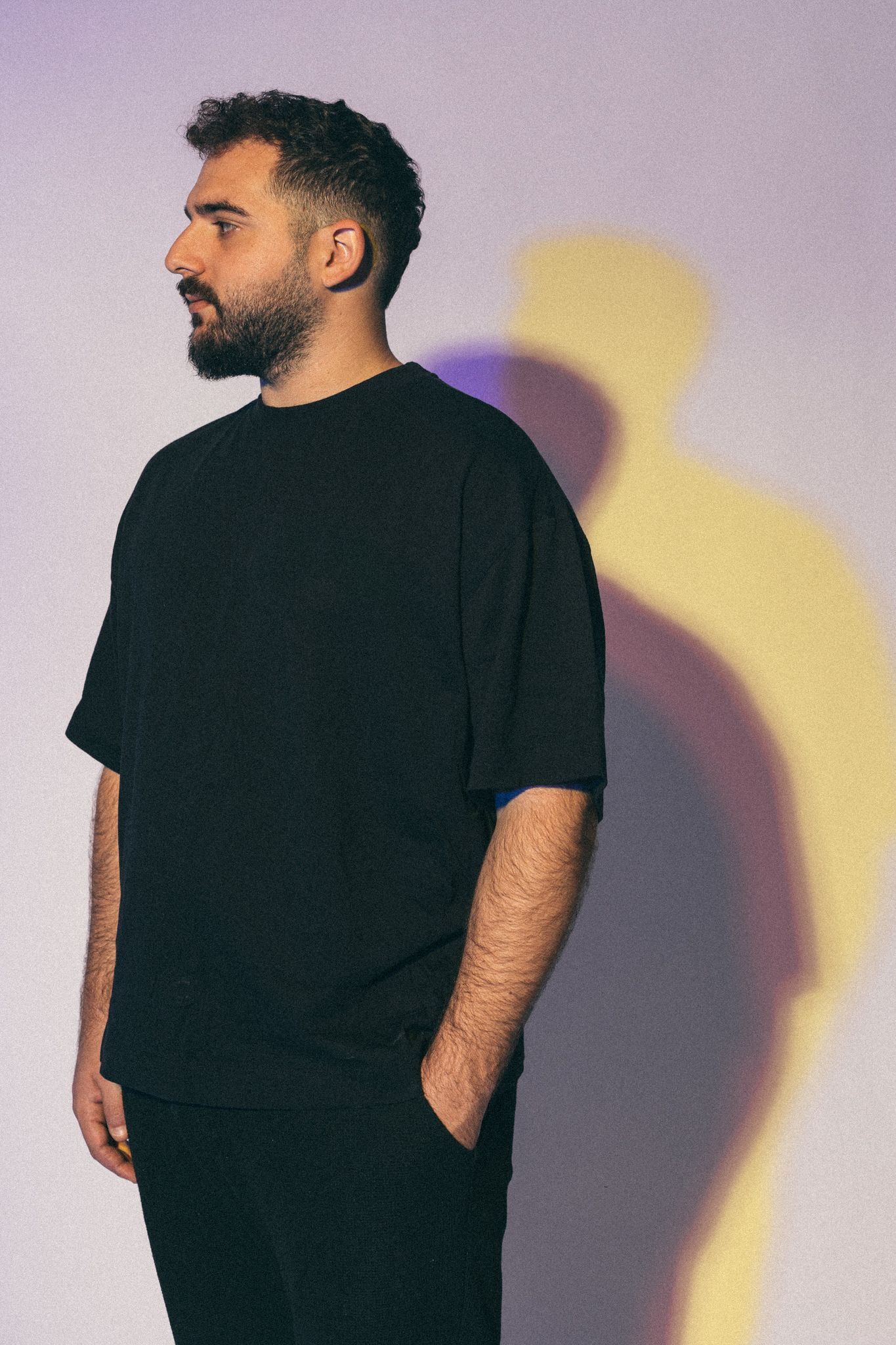 Side profile portrait of person in black t-shirt against purple wall with yellow shadow.