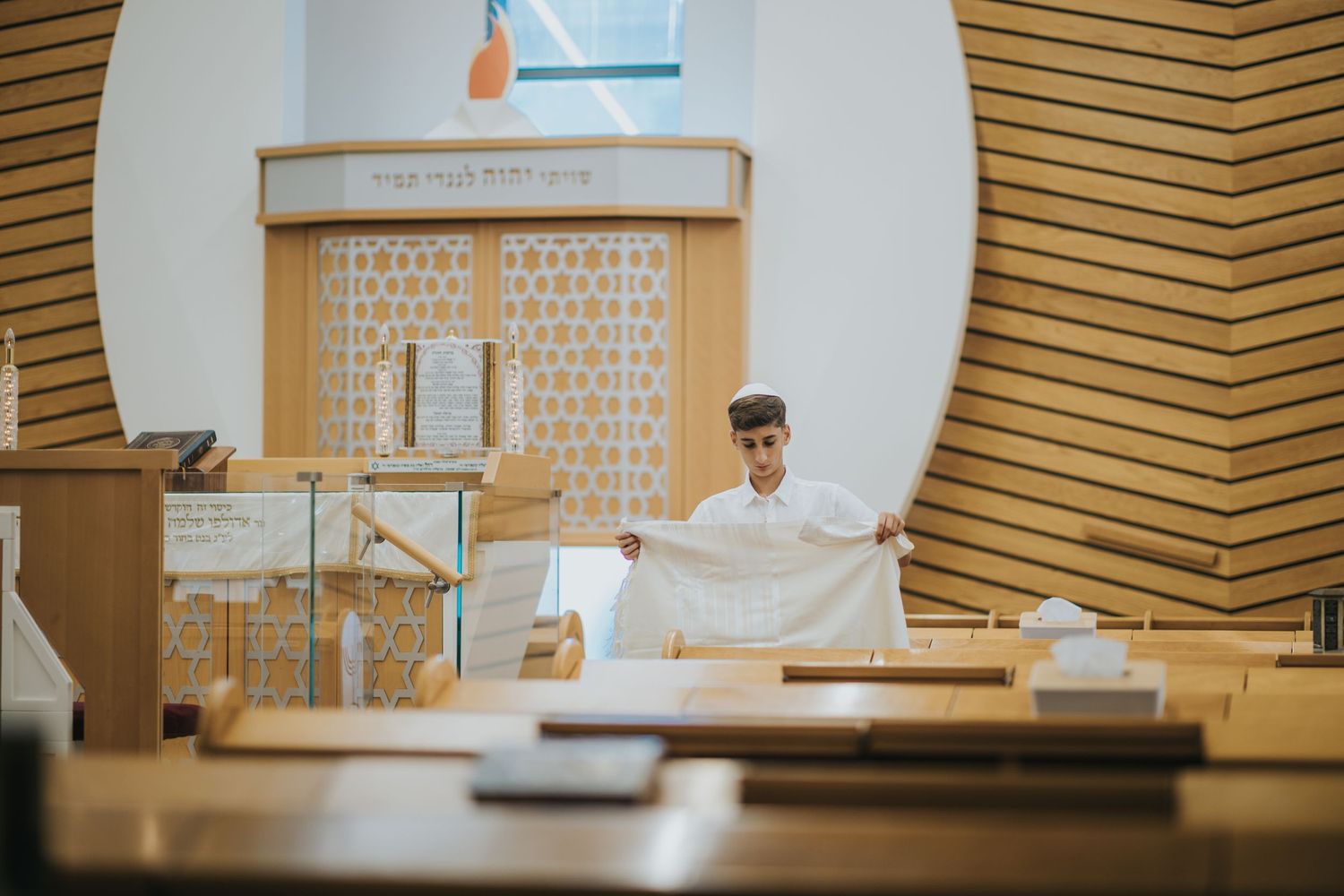 Someone wearing religious garments stands at a synagogue podium preparing for service.