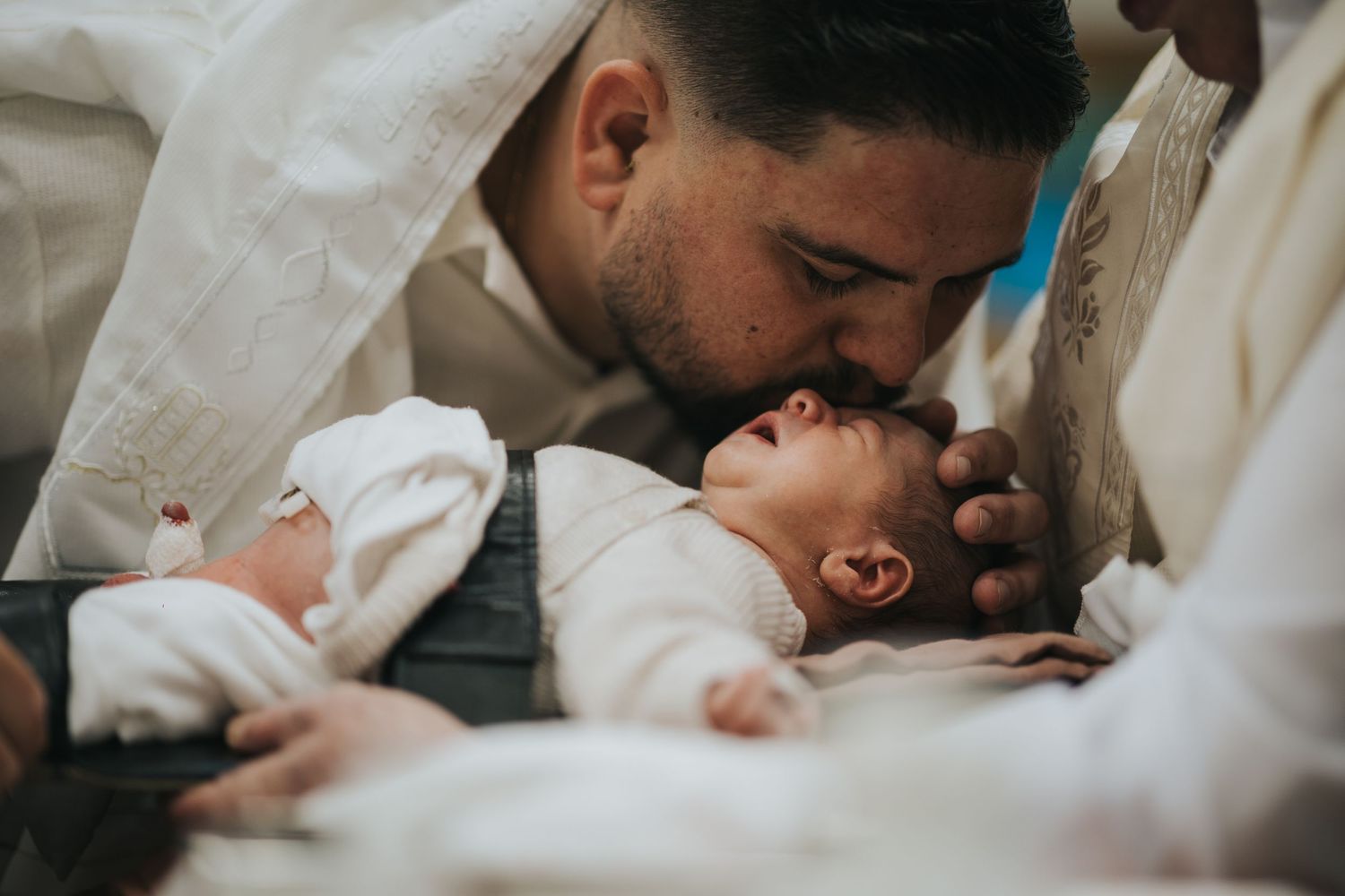Intimate moment during a baby ceremony with white traditional clothing and soft lighting.