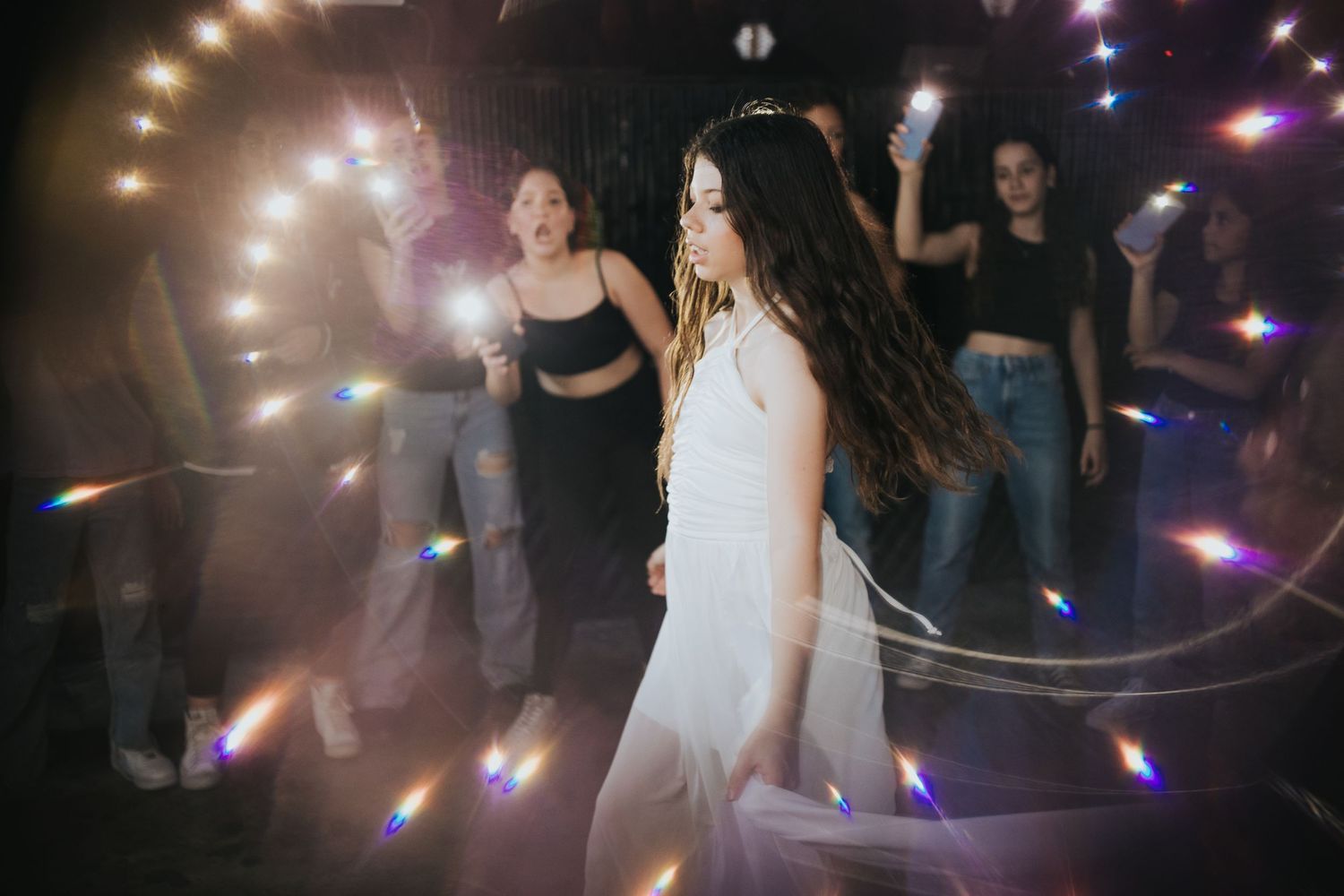 Dance party scene with lighting effects and multiple people celebrating in a dark venue.