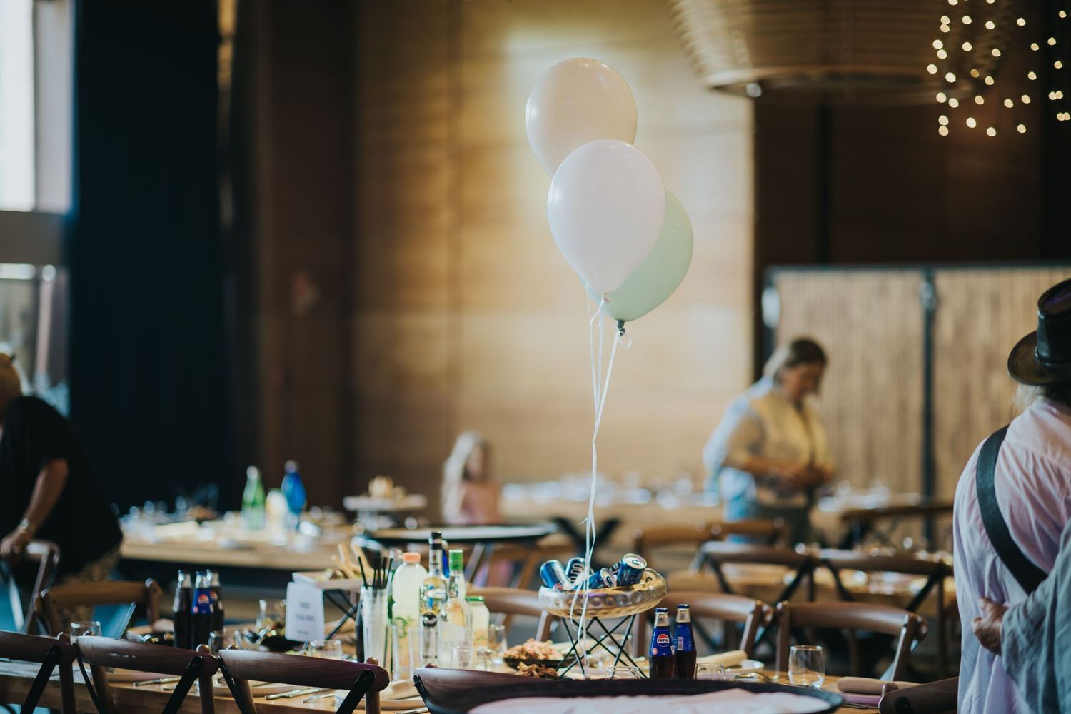 Reception table settings with floating balloons and soft ambient lighting in an indoor venue.