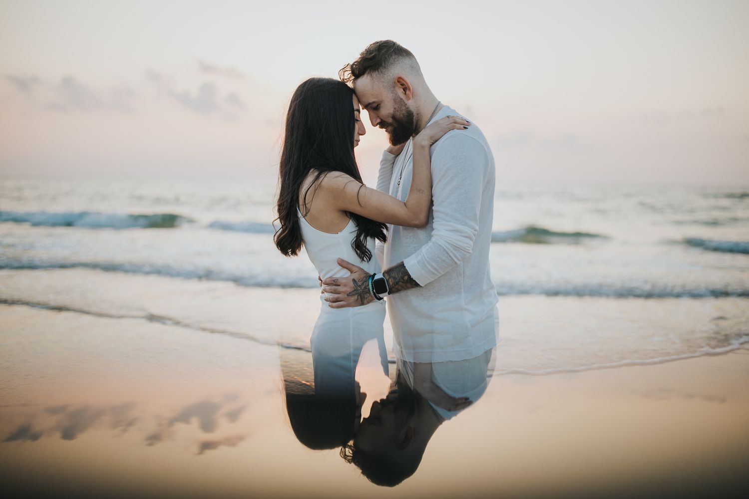 A romantic couple embraces on the beach during golden hour.