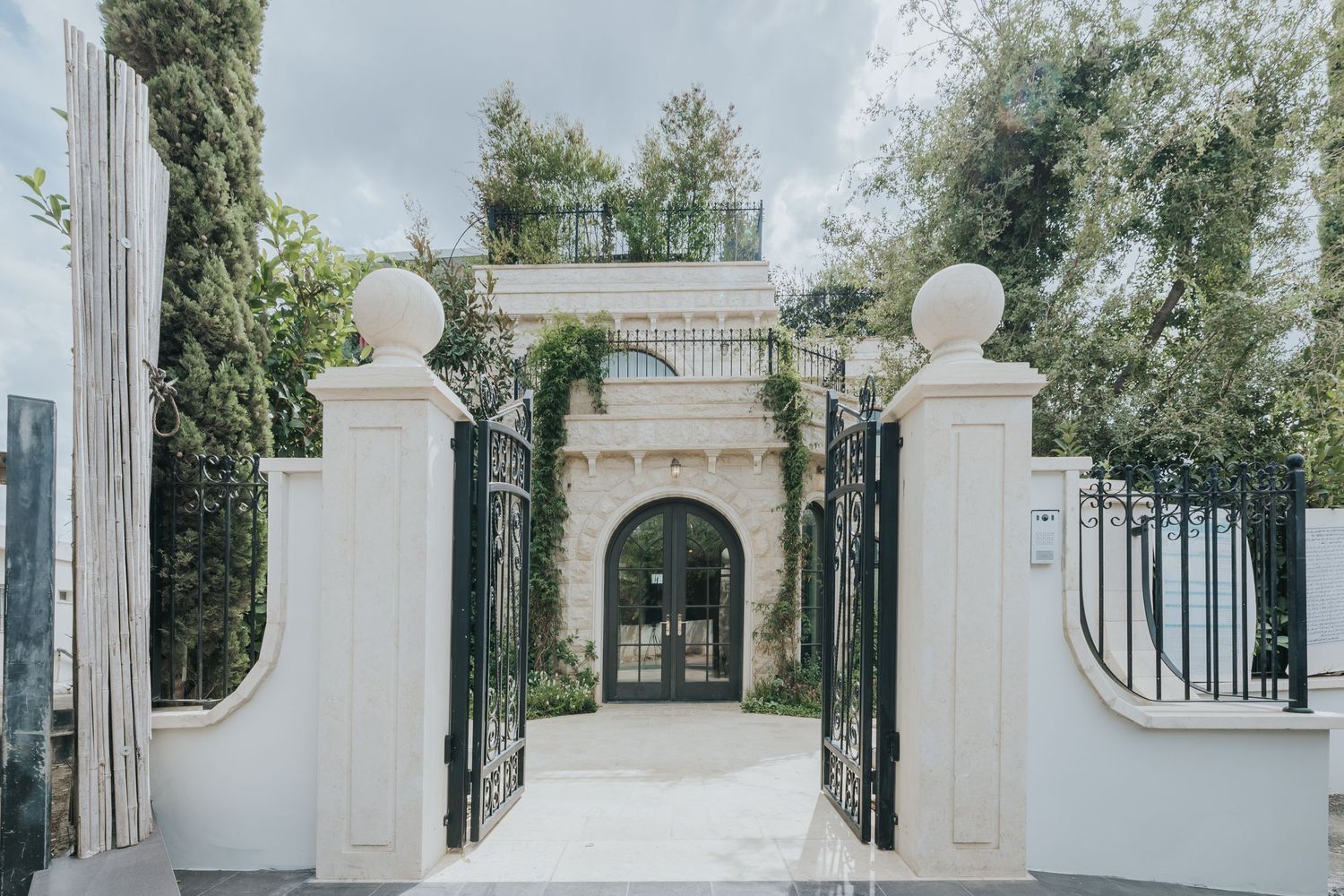 White Mediterranean archway with ornate pillars and iron gates leading to garden pathway.