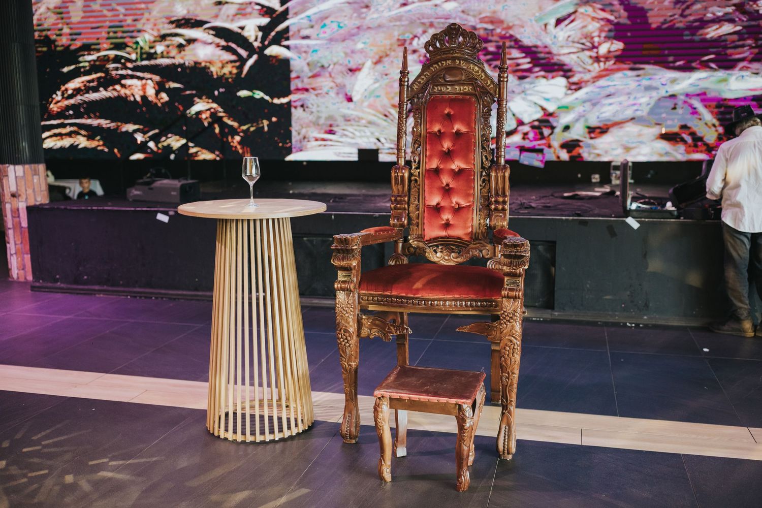 Ornate gold throne chair and modern pedestal table setup against dark walls with pink lighting effects.