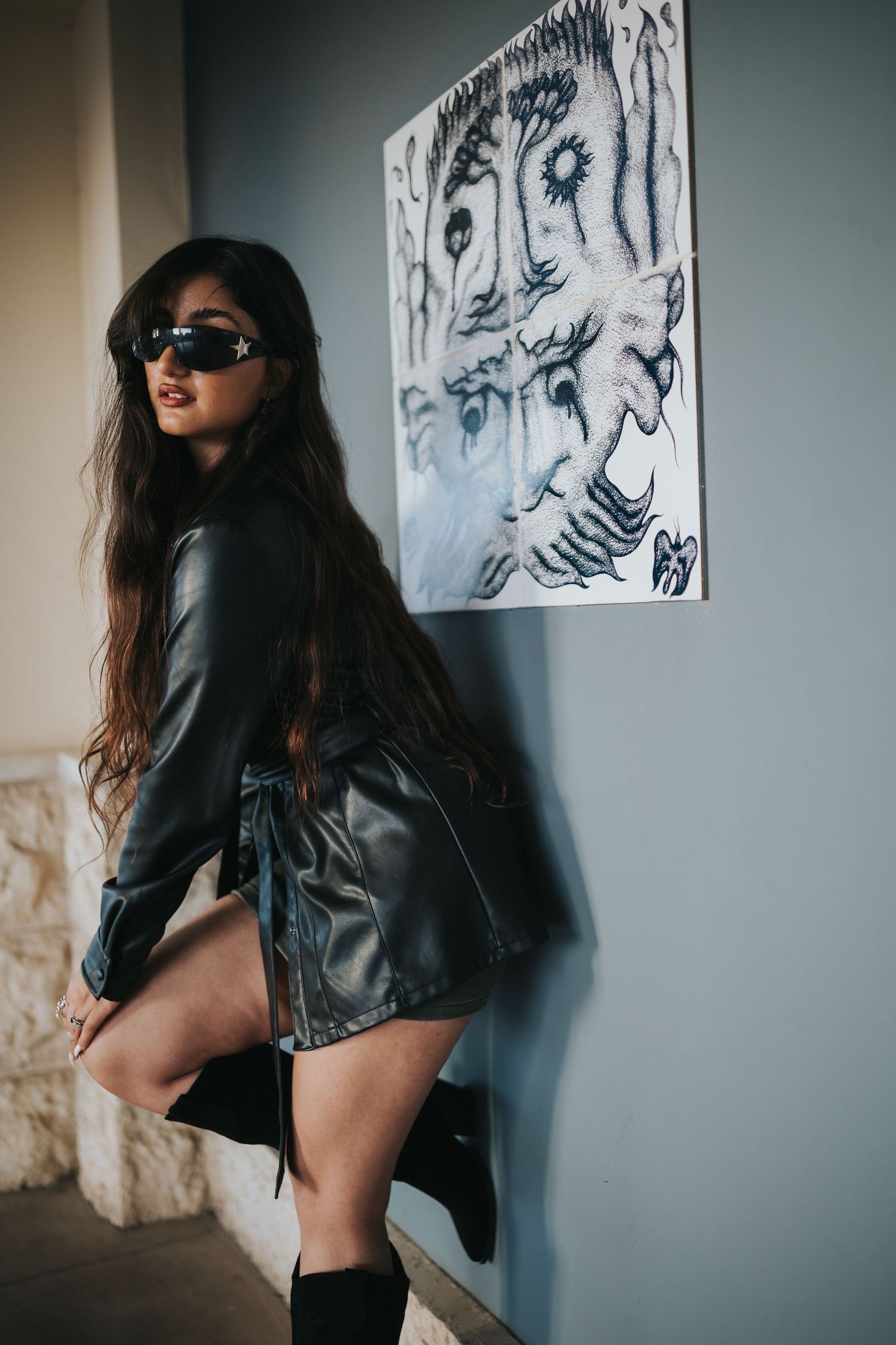 Fashion portrait with sunglasses against wall with abstract black and white artwork.
