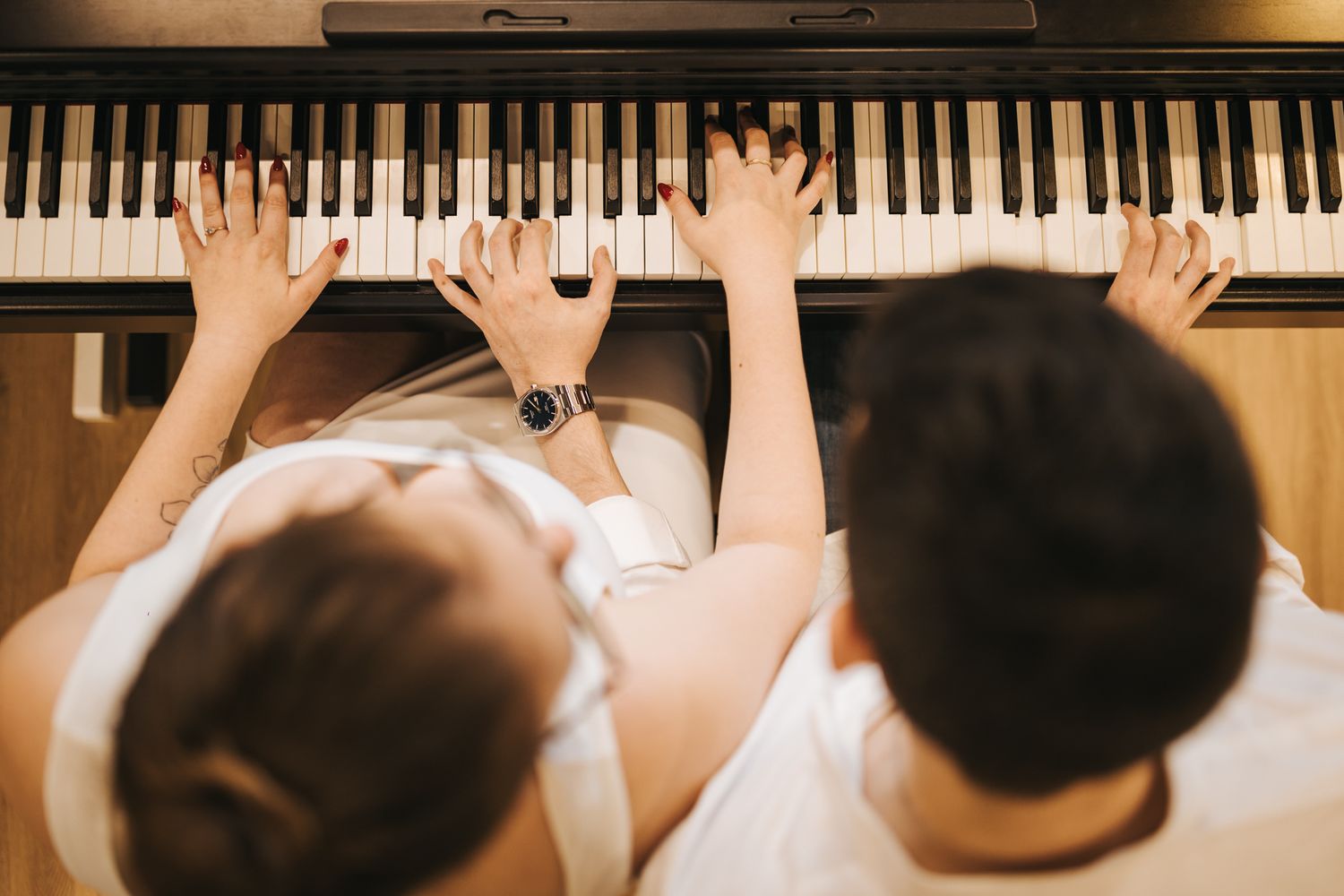 Overhead view of hands playing piano duet on black and white keys.