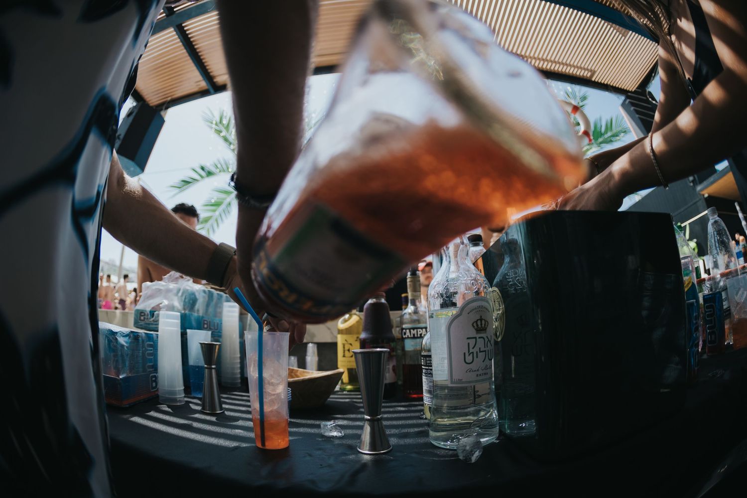 Bartender pouring cocktail captured through fisheye lens at busy bar.