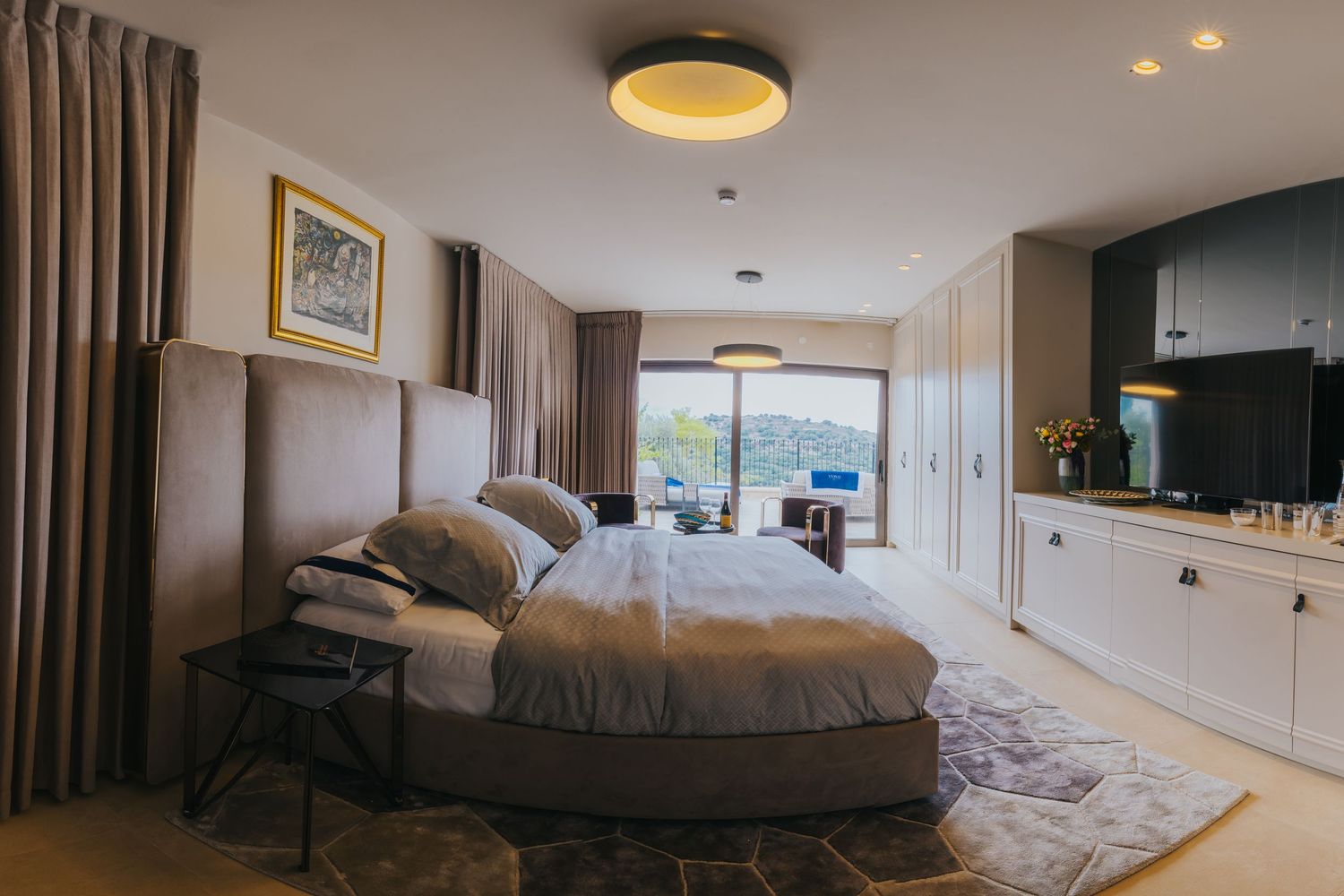 Modern hotel bedroom with panoramic windows offering mountain views and contemporary neutral decor.
