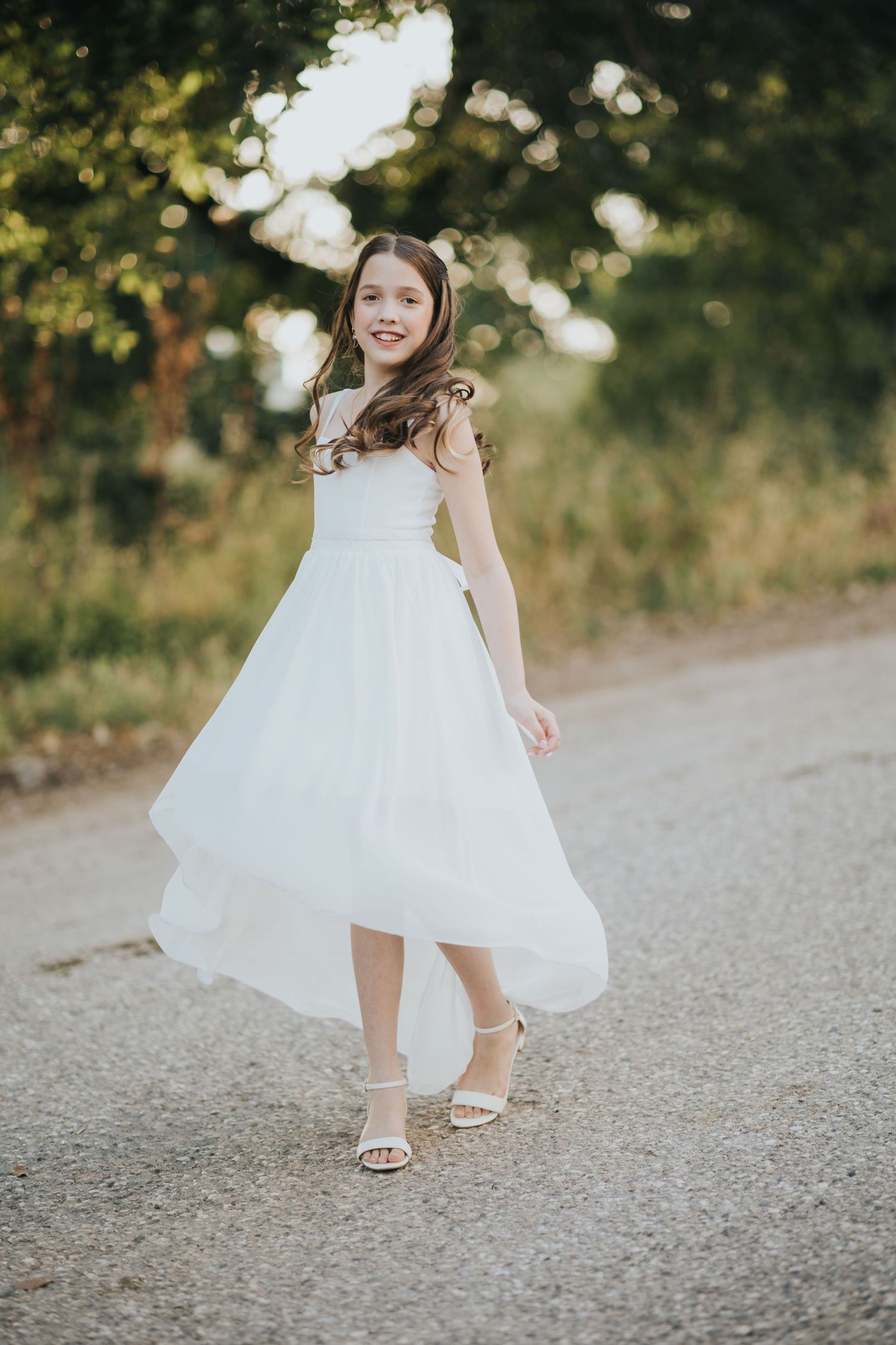 Joyful twirling movement in a white dress on a sunlit path.