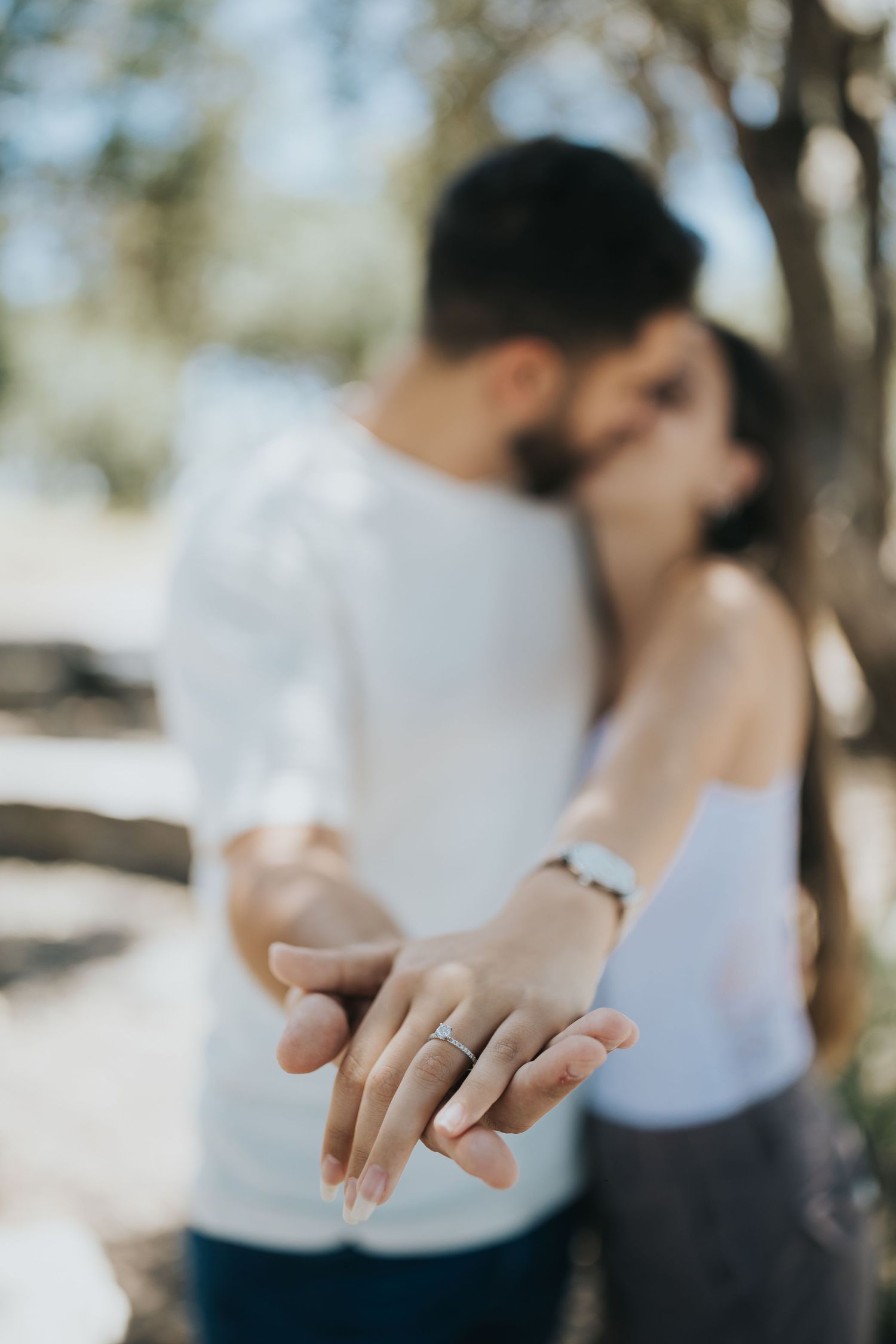 Close-up of engaged couple's hands showing off engagement ring in natural sunlight.