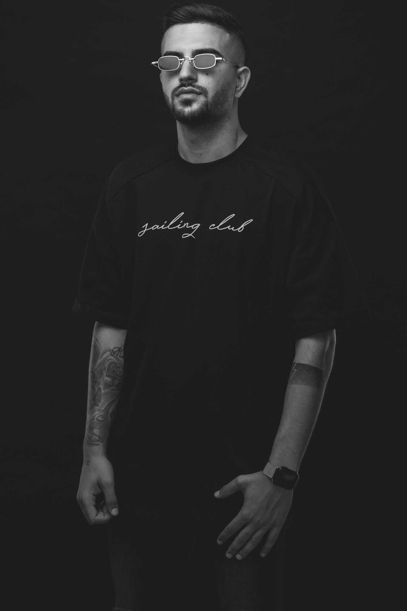Artist wearing glasses and black graphic t-shirt poses for black and white portrait.