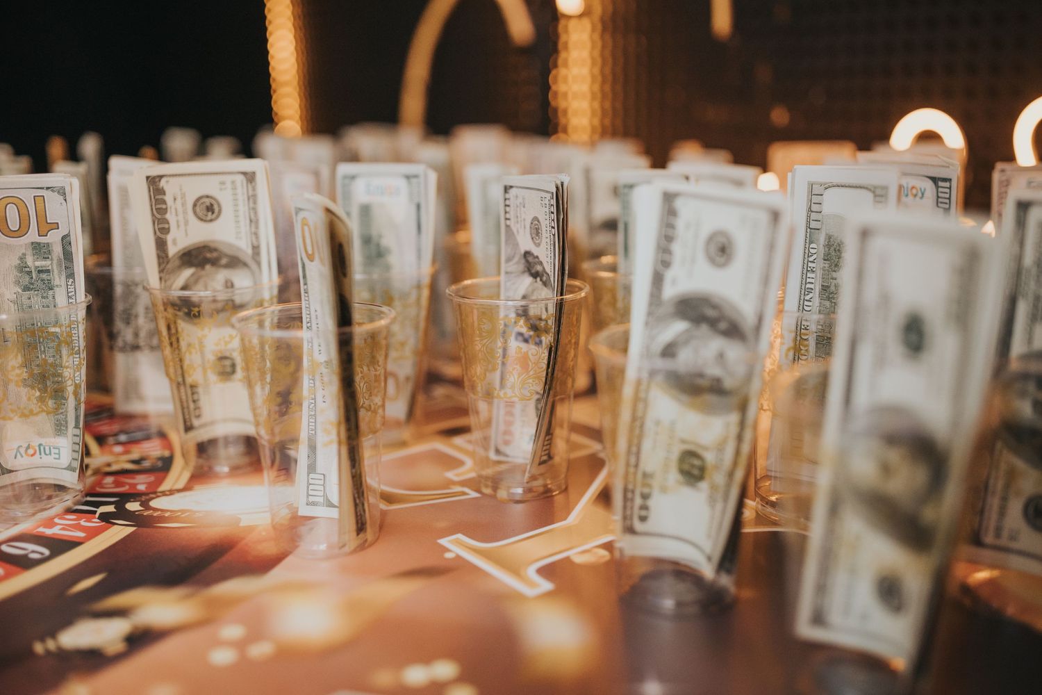 Multiple US dollar bills arranged standing upright on reflective surface with warm lighting.
