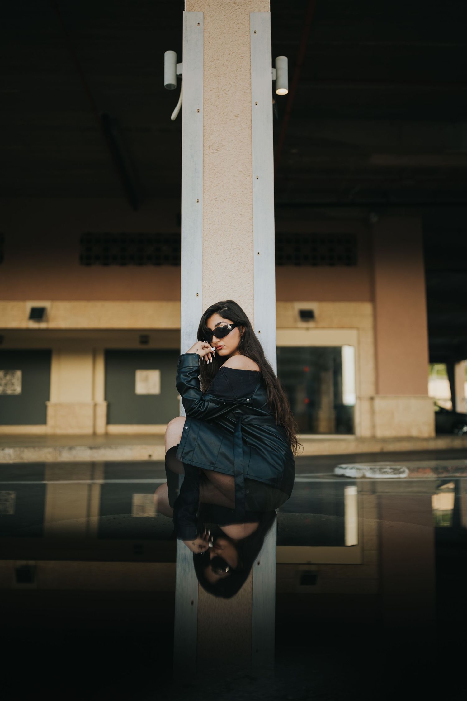 Stylish portrait with dramatic reflection featuring long dark hair and sunglasses against column.