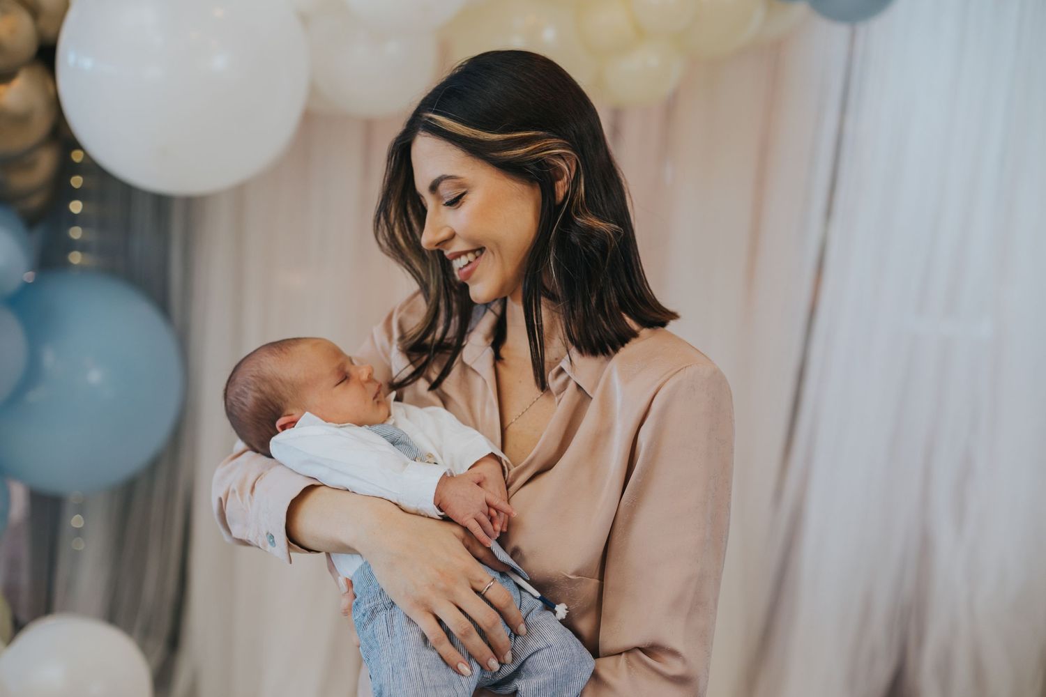 Tender moment with baby at celebration decorated with blue and white balloons.