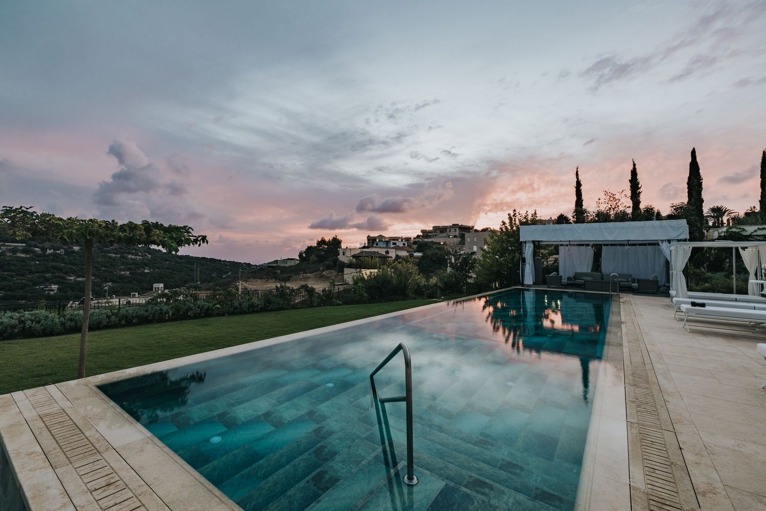 Stunning infinity pool with turquoise water against pink sunset sky and cypress trees.
