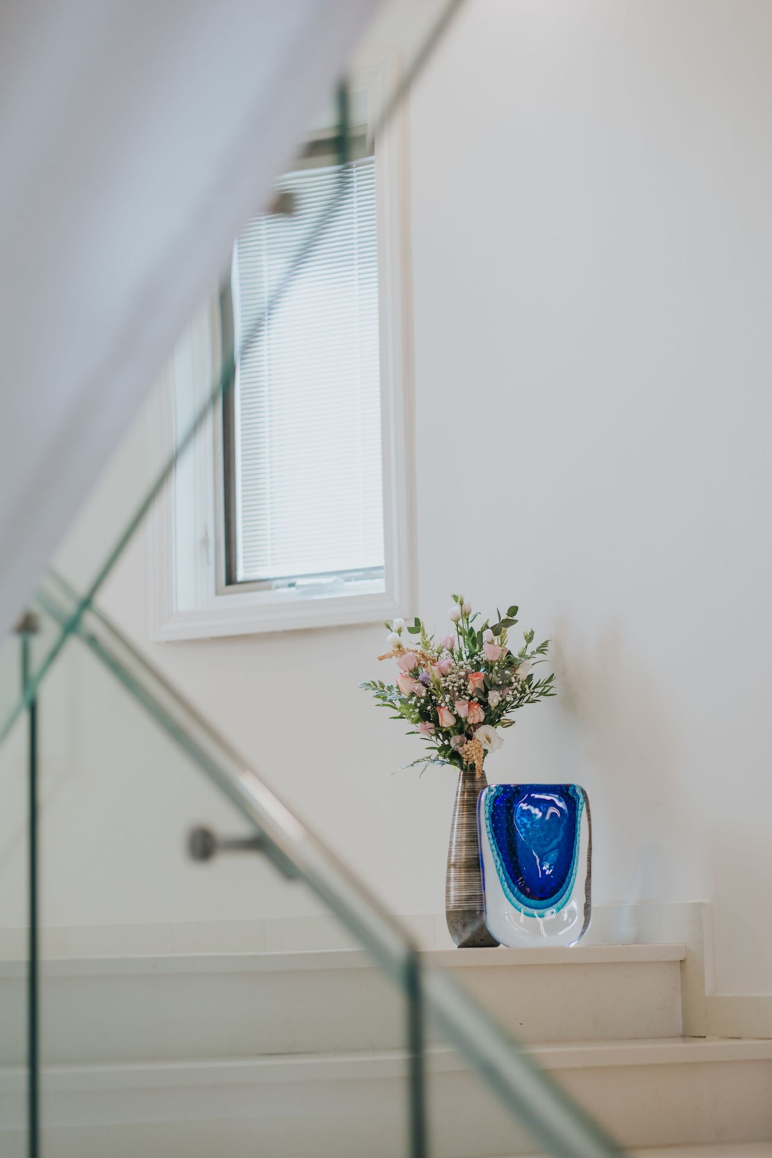 Elegant staircase with glass railing decorated with fresh floral arrangement and blue glass accent piece.