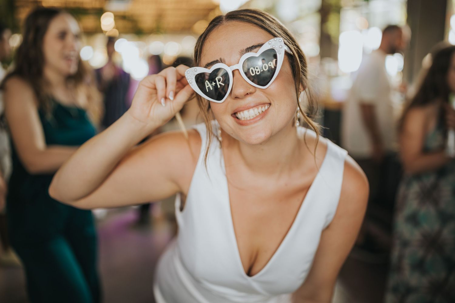 A person in a white dress wearing heart-shaped sunglasses smiles during a celebration.