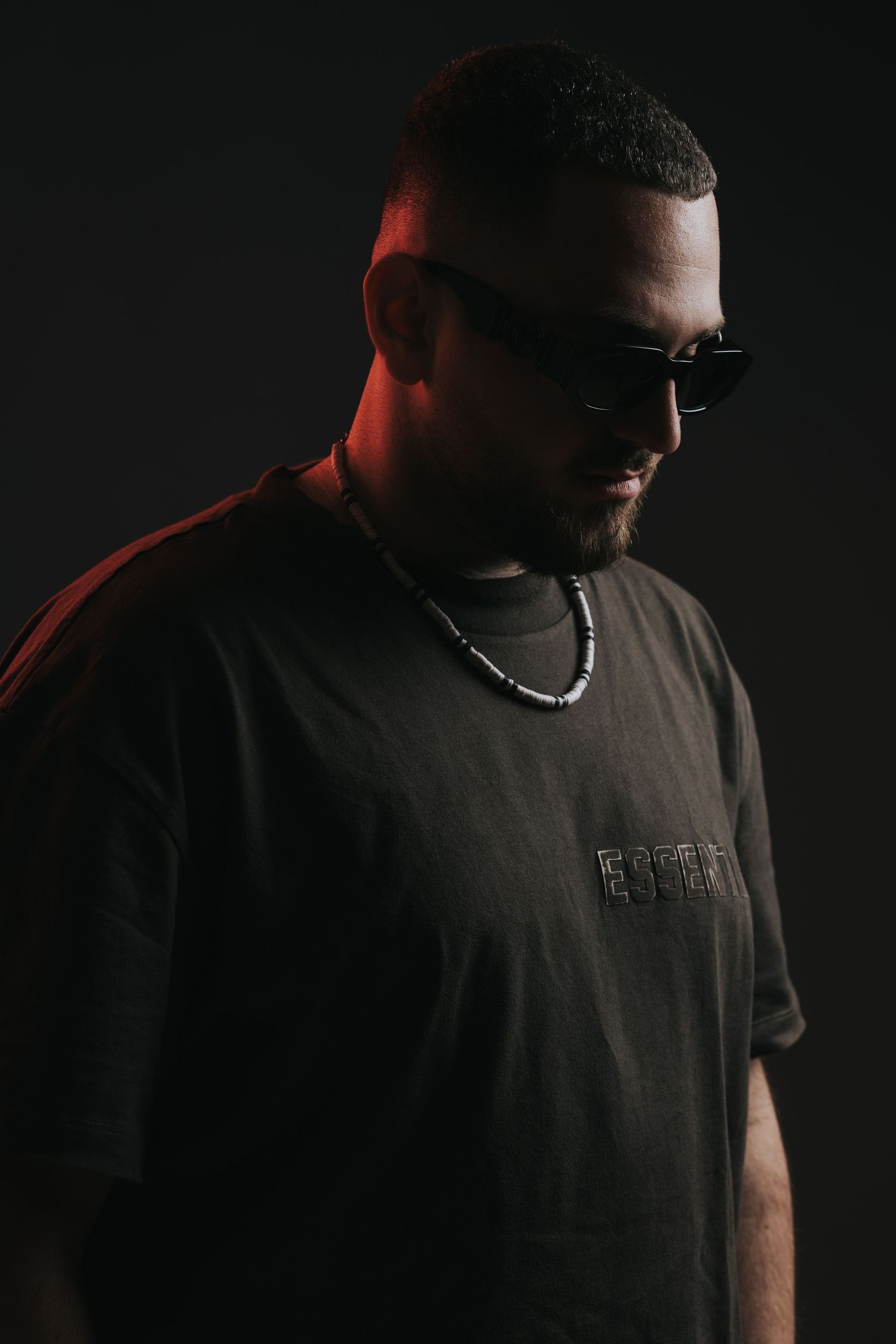 Moody portrait of person in dark t-shirt and sunglasses with dramatic side lighting.