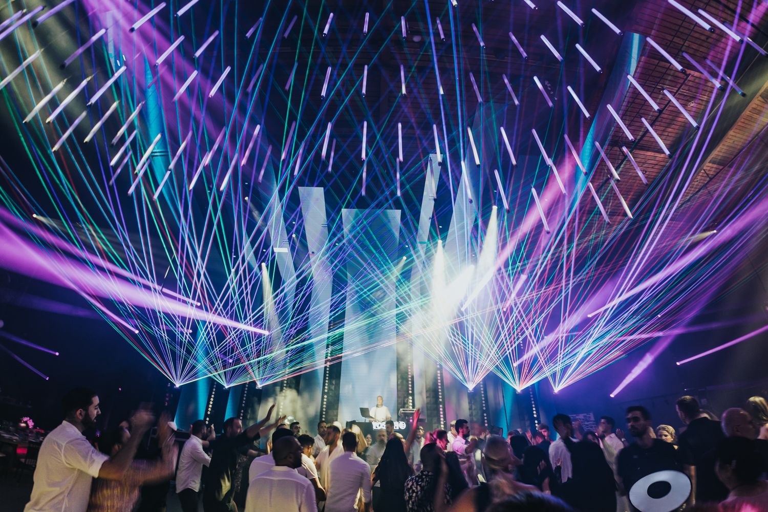 Spectacular laser light show illuminating a crowded dance floor with vibrant purple and blue beams.