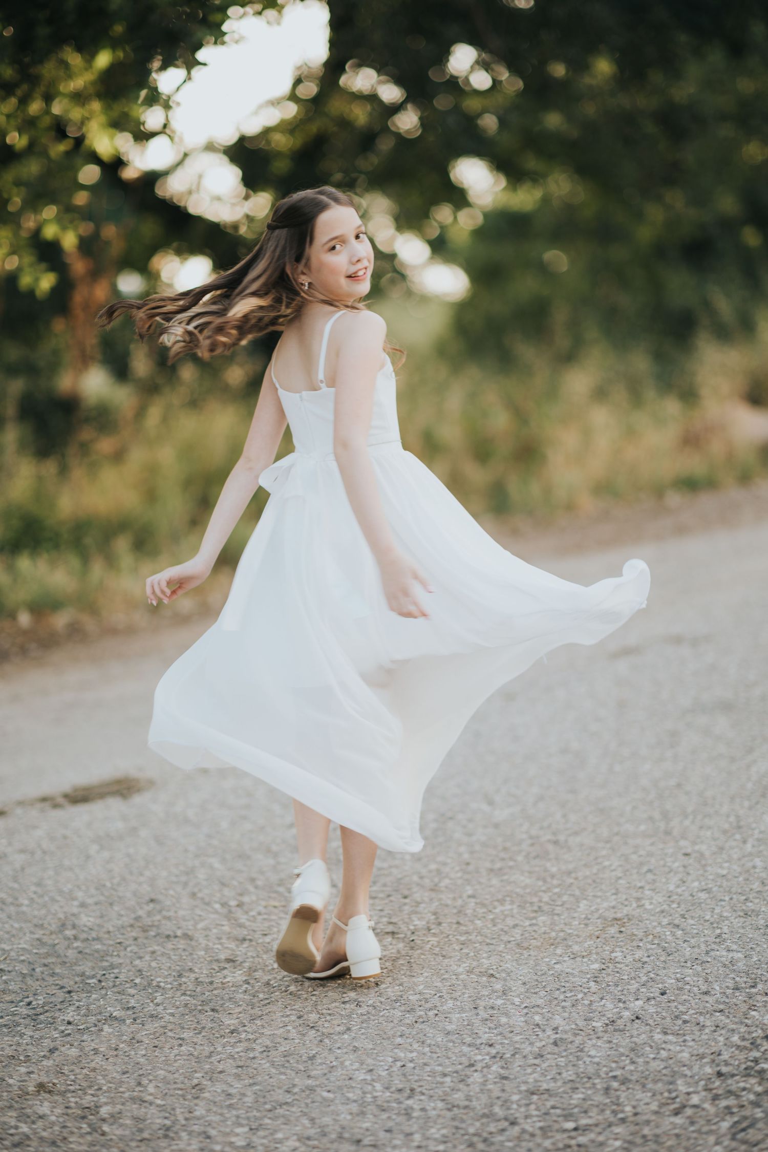 White dress twirling on a sunny path with natural bokeh effect.