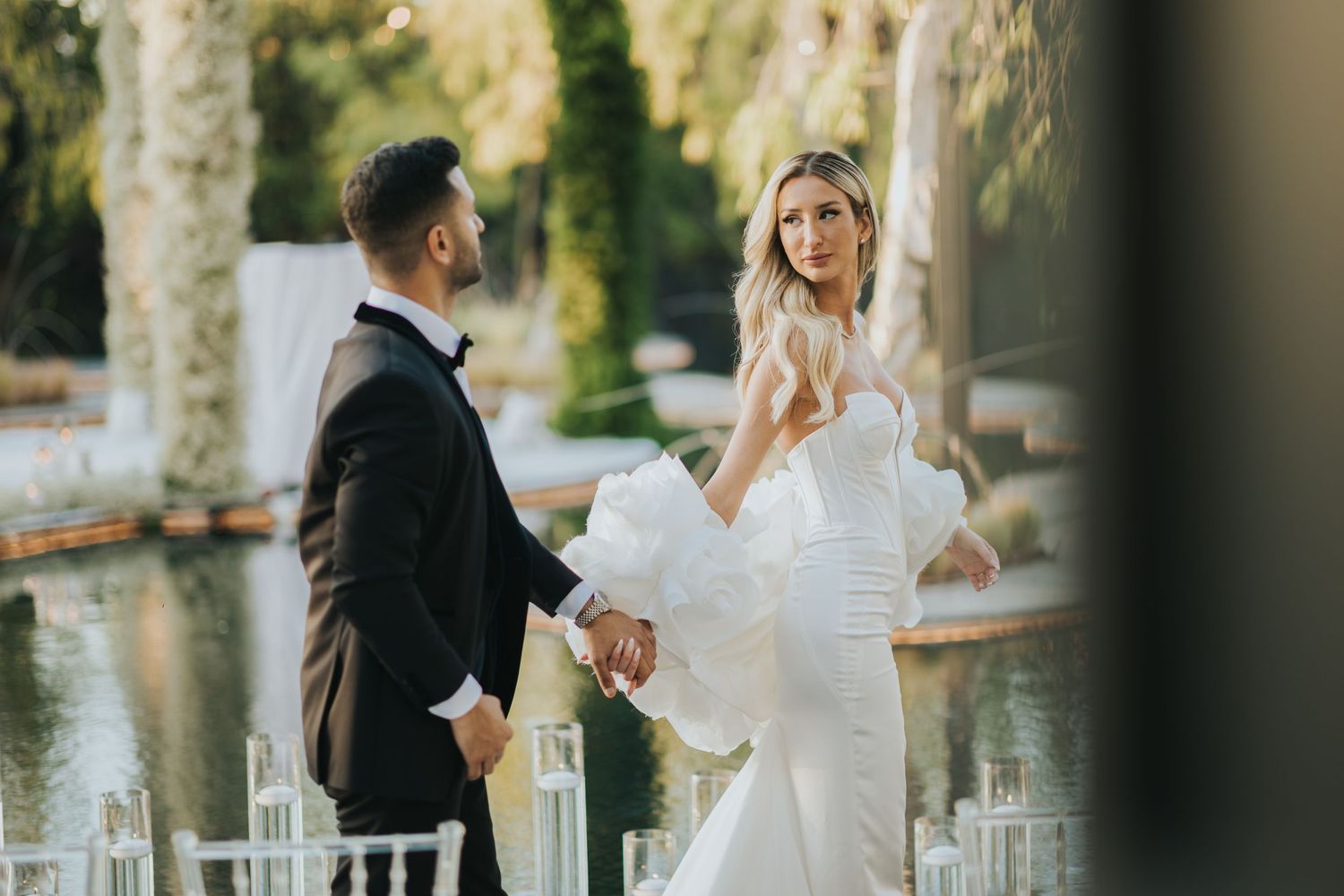 Couple in formal attire sharing playful moment at outdoor wedding reception.