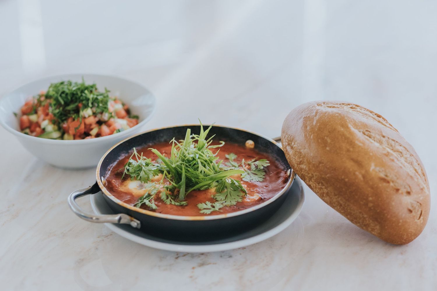 Hot soup dish with fresh herbs and crusty bread served on white tablecloth.