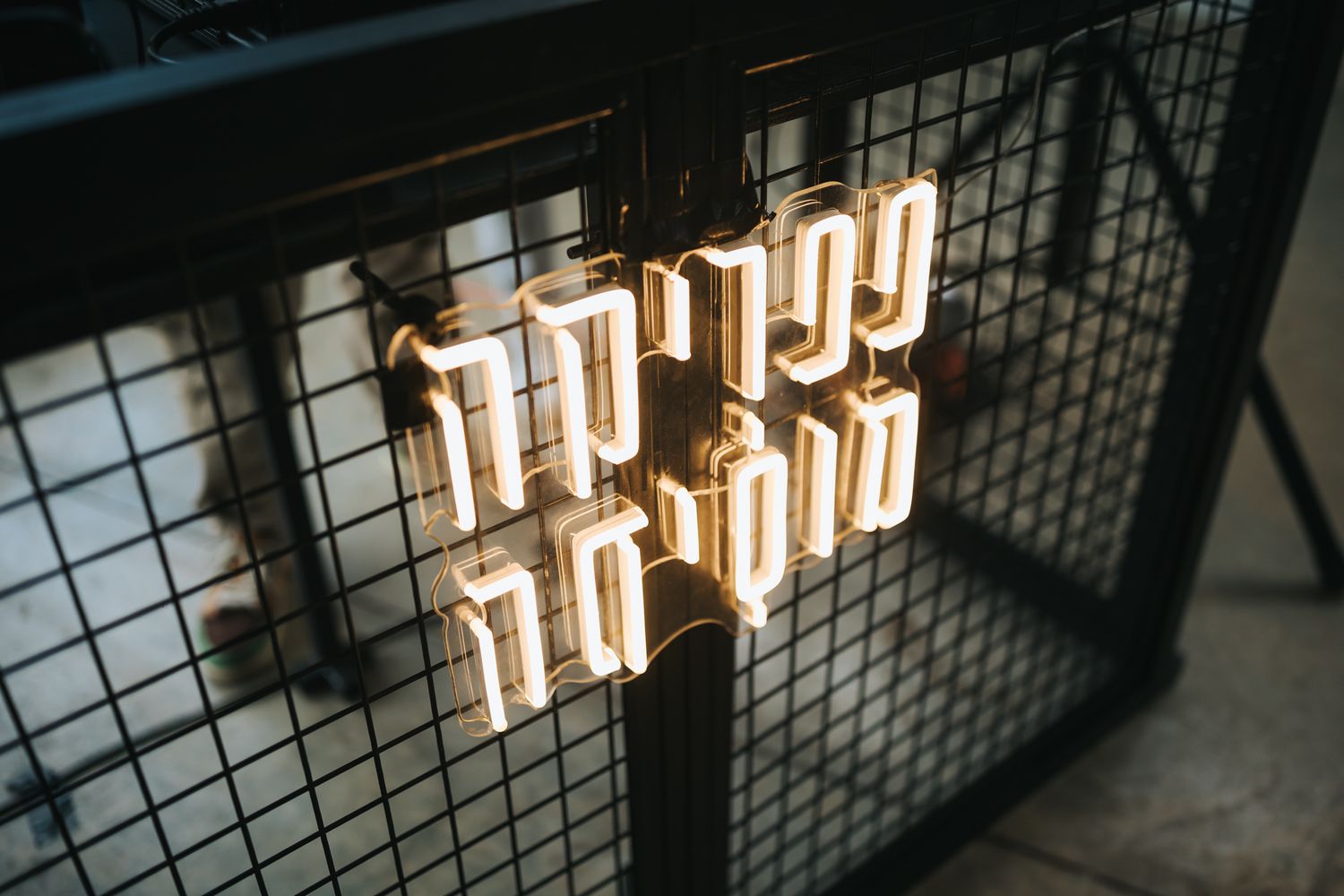 Neon typography sign mounted on industrial mesh wire background.