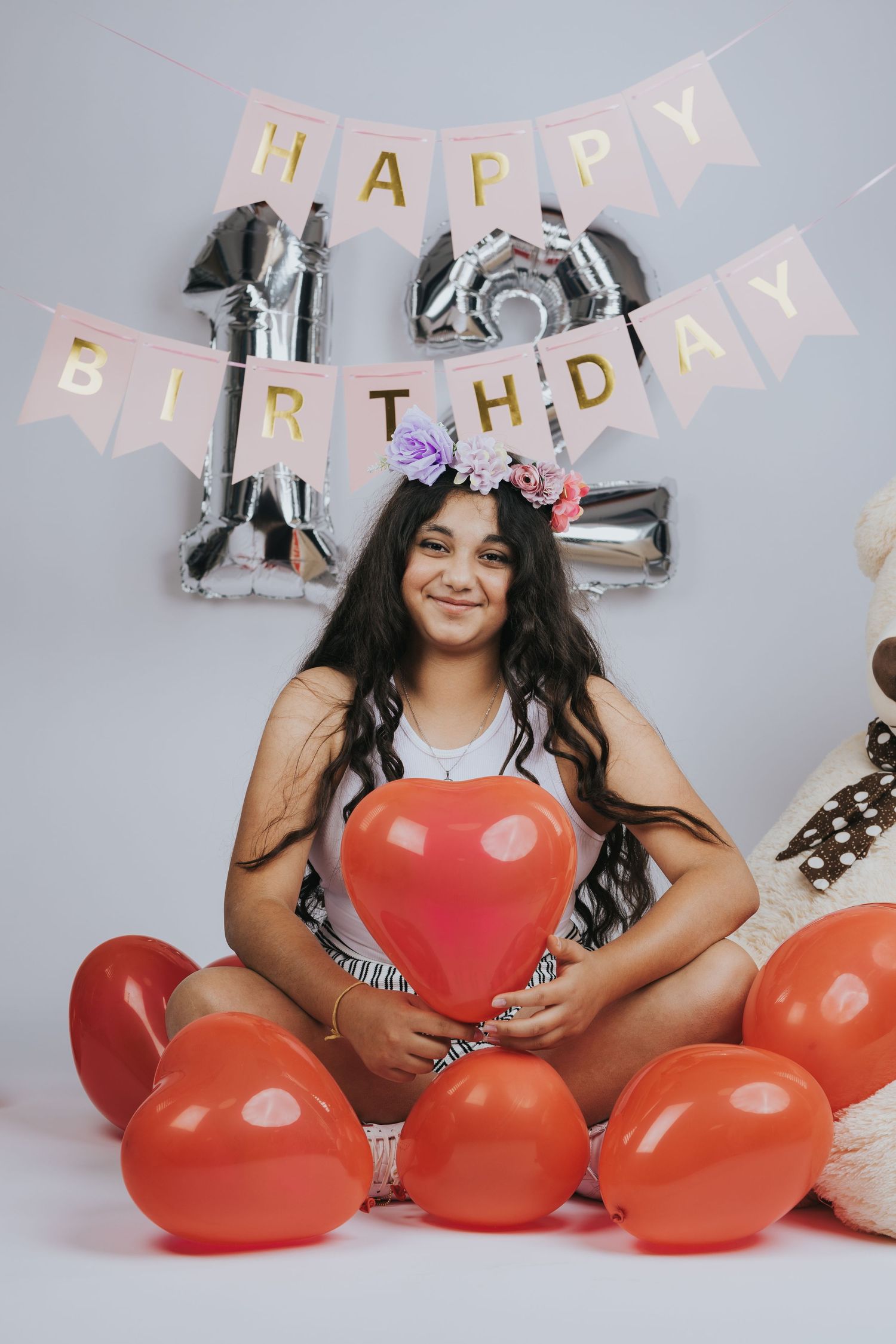 Birthday celebration setup with silver number balloons, red heart balloons and a festive 'Happy Birthday' banner on grey background.
